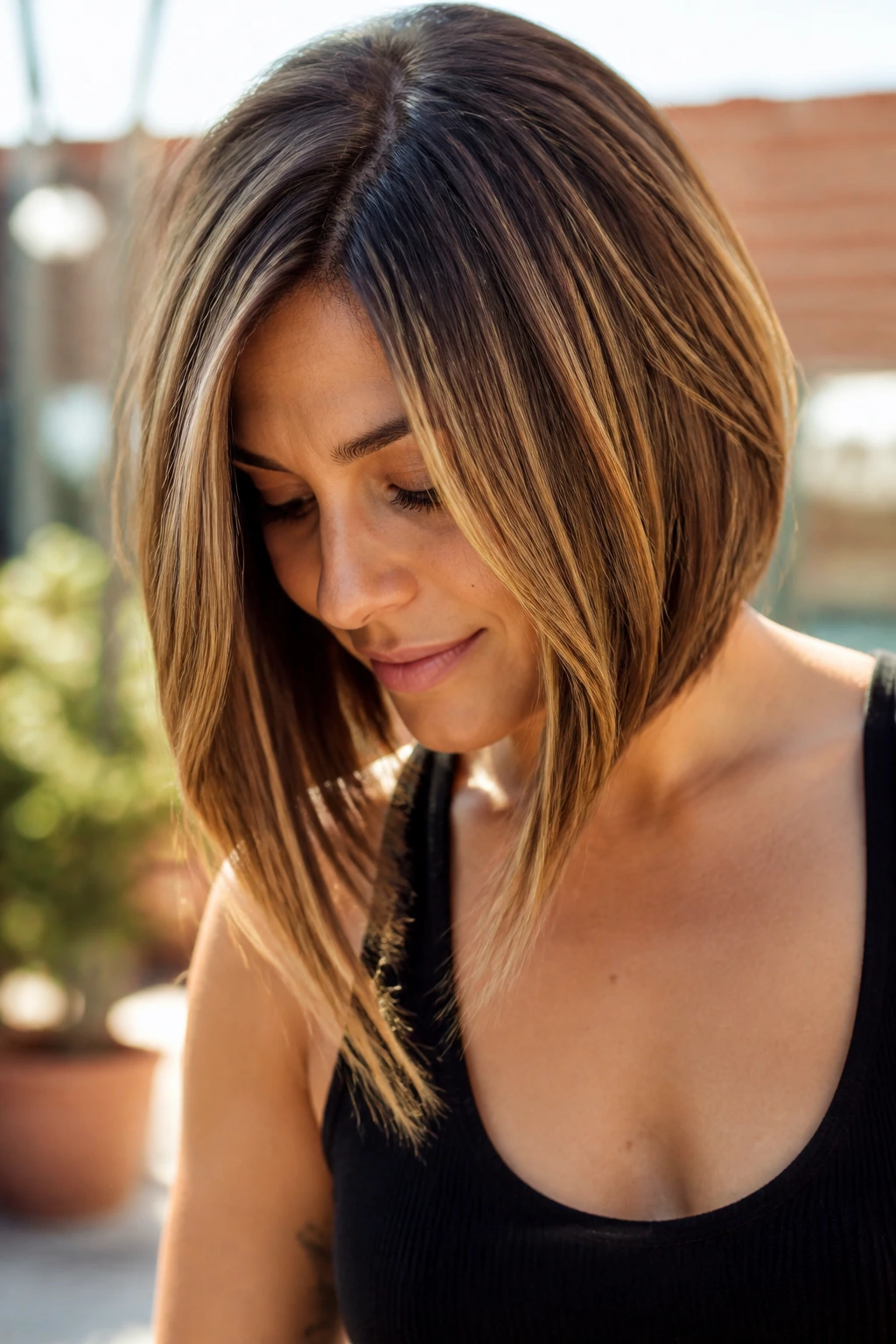 Close-up portrait of a real woman with angled face-framing lob on a sunlit outdoor terrace