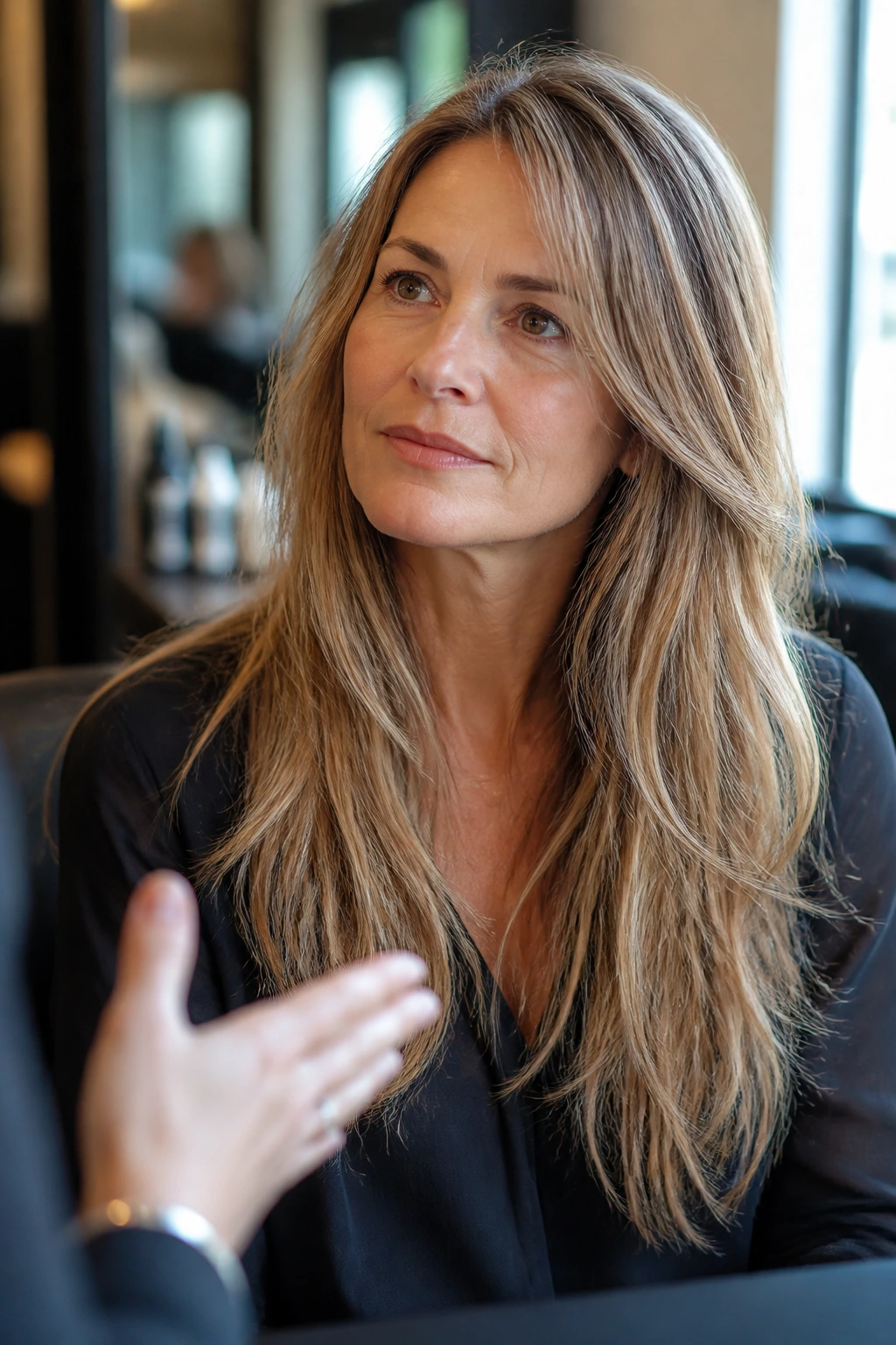 Portrait of a real woman with long fine hair and babylights in a salon, thoughtful consultation