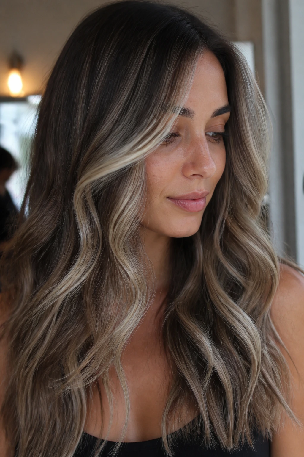 Brunette with ash beige balayage in long waves under cool lighting