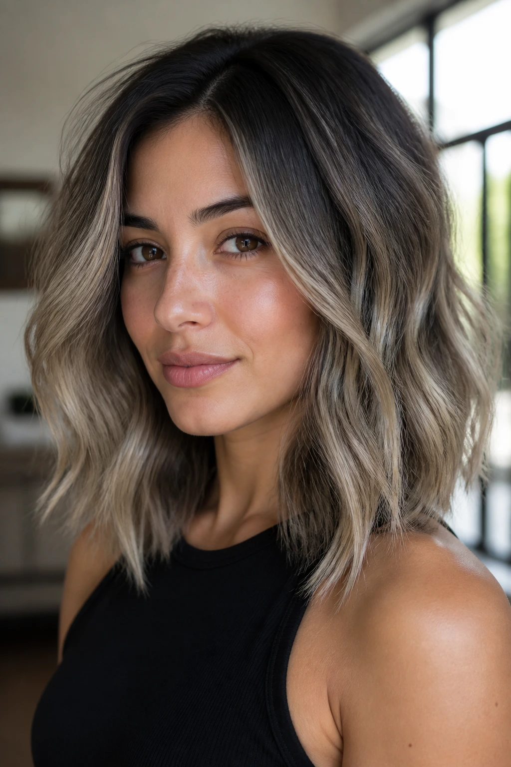 Close-up portrait of a real woman with ashy balayage and shadow melt on shoulder-length wavy hair, natural window light