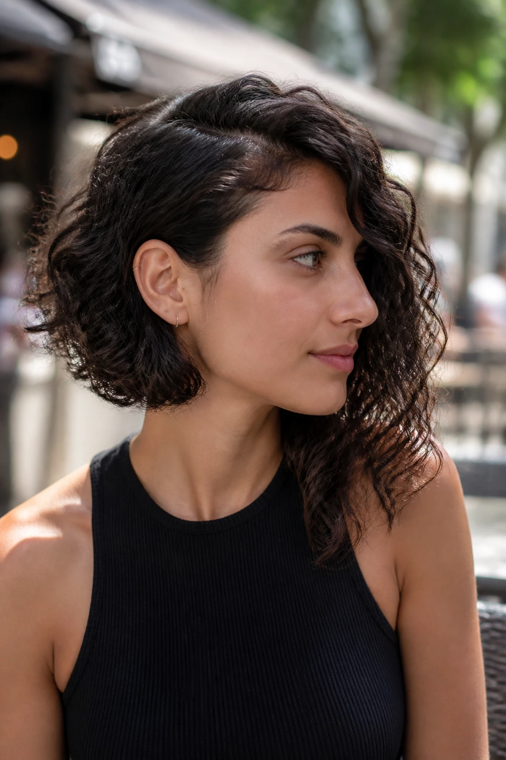 Real woman with an asymmetrical curly lob, one side longer, in daylight at a street cafe.