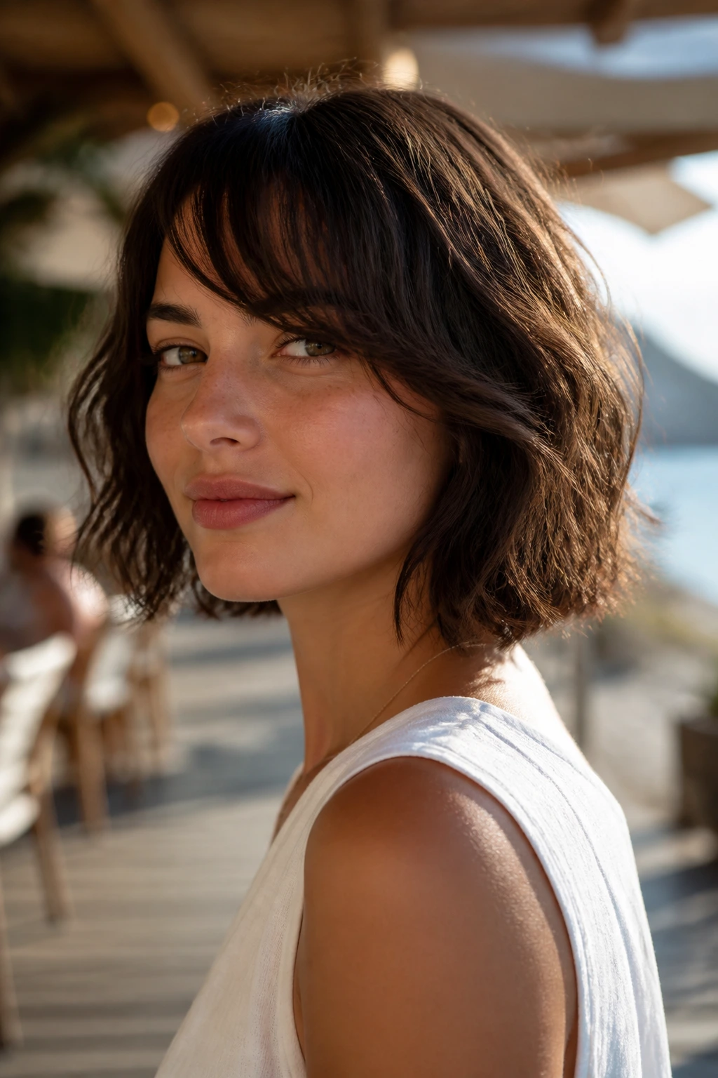 Close-up of a real woman with a beachy air-dry bob and waves against a sunlit seaside setting