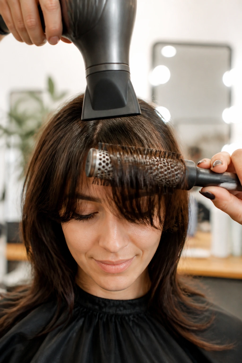 Close-up person with bangs being styled using essential tools in a bright setting.