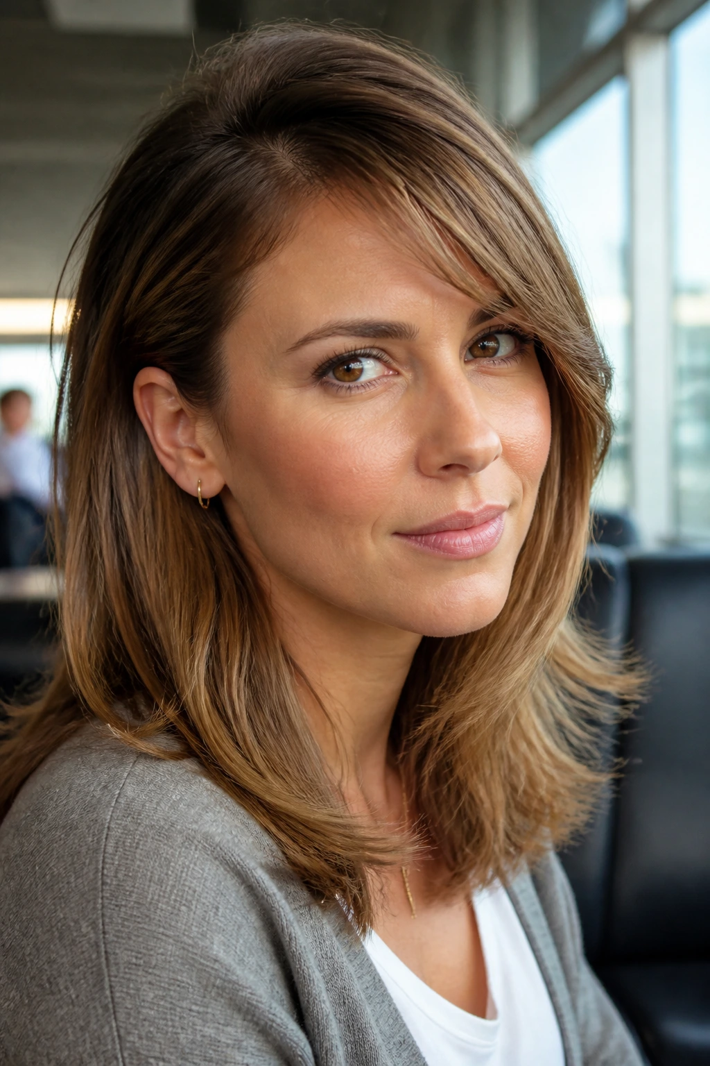 Close-up portrait of a real woman with tucked-behind-ear blowout and side-swept bangs in an airport lounge