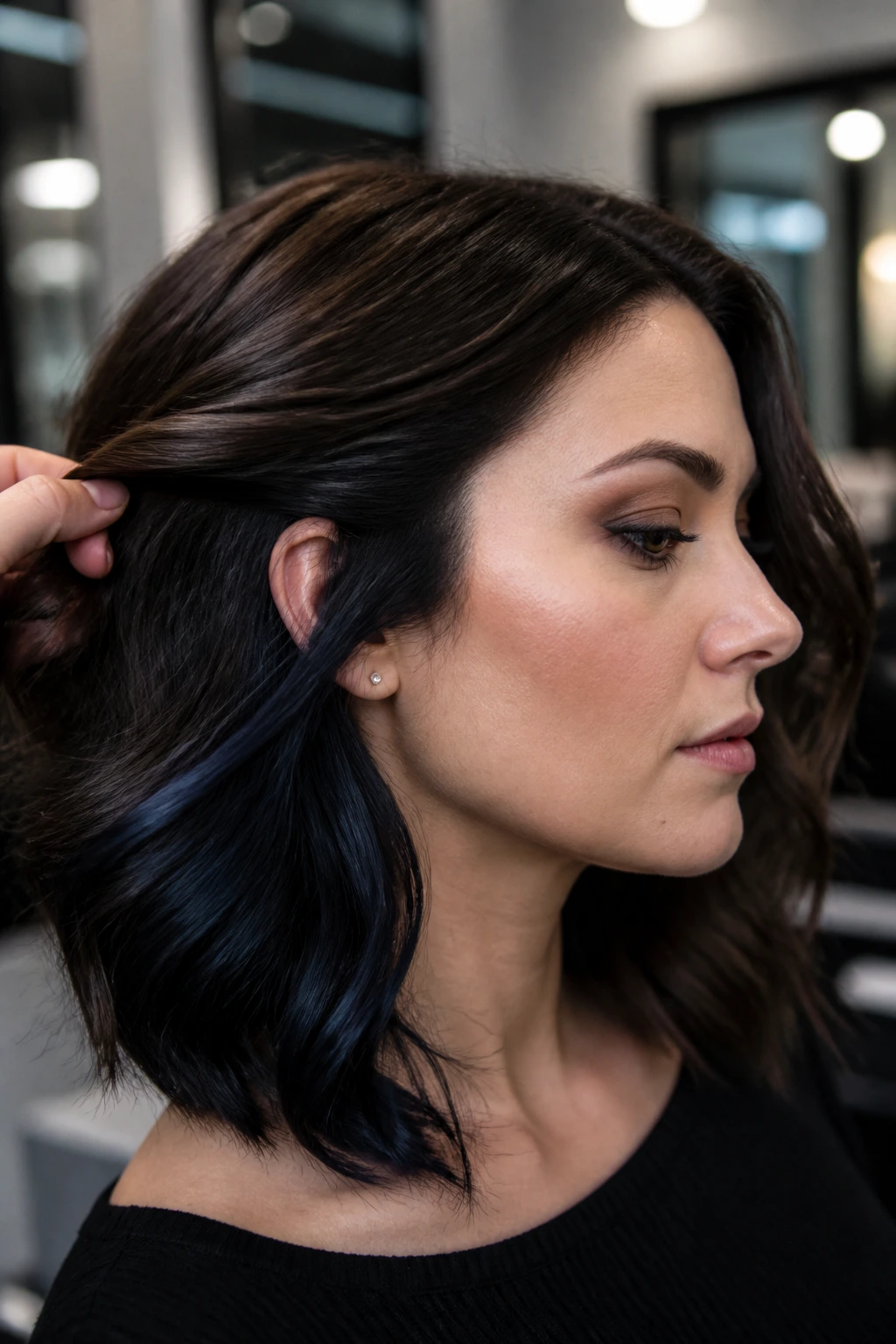Close-up portrait of brunette with blue-black underlights peeking through hair in a cool-toned salon