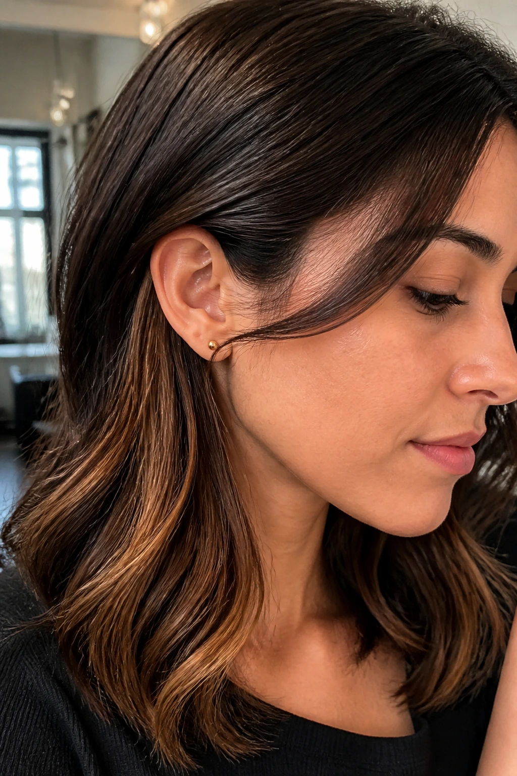 Close up portrait of a real woman showing bronze peekaboo layers peeking from brunette hair in soft window light