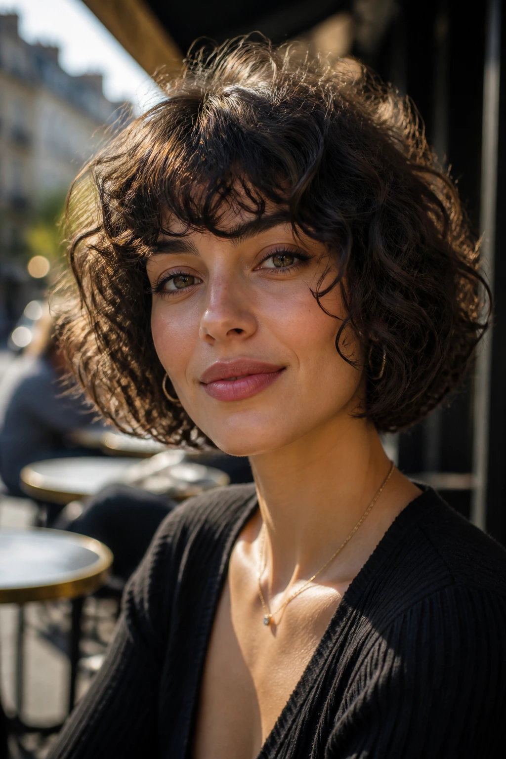 Portrait of a woman with brow-grazing French bob and loose curls on a heart-shaped face.