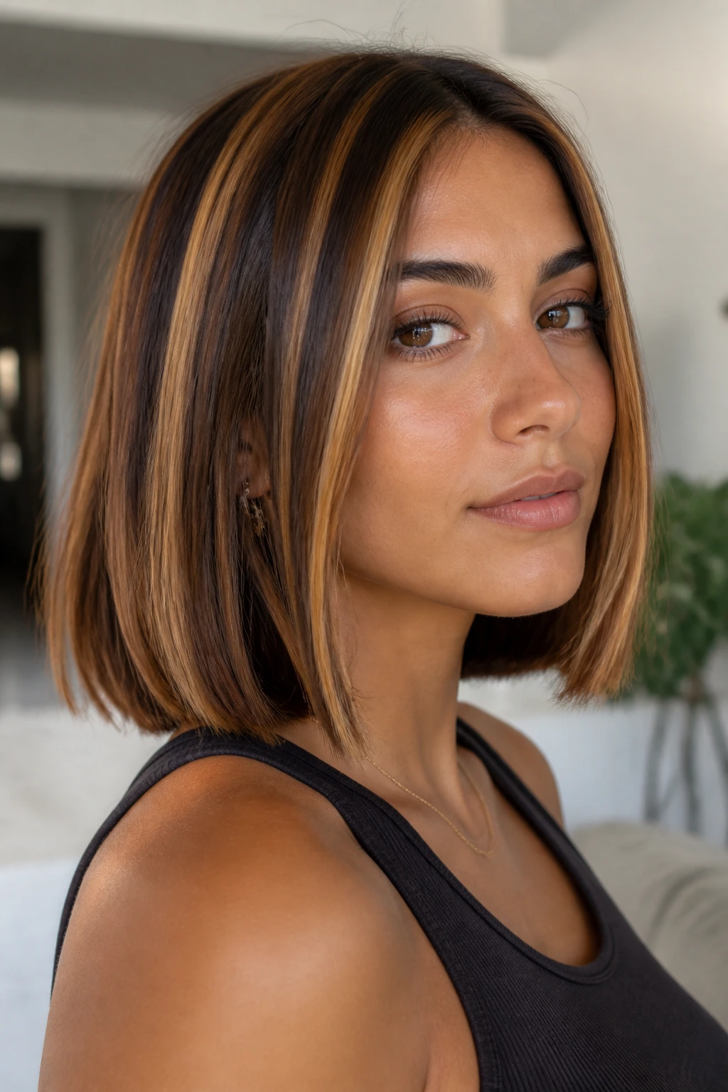Close-up of a real woman with chunky caramel stripes on olive skin hair, warm interior.