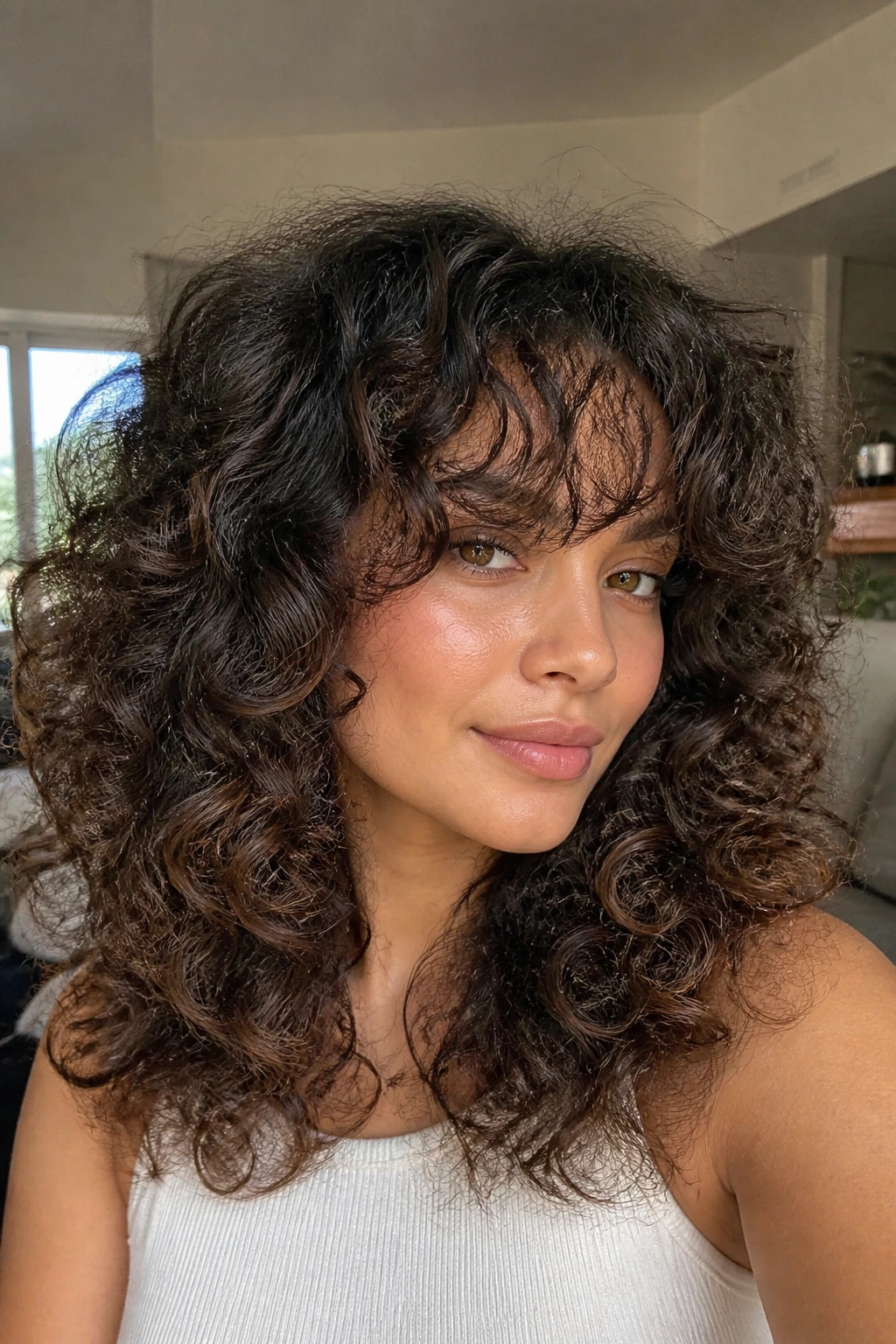Close-up of a real woman with voluminous curls and wispy bangs in soft natural light