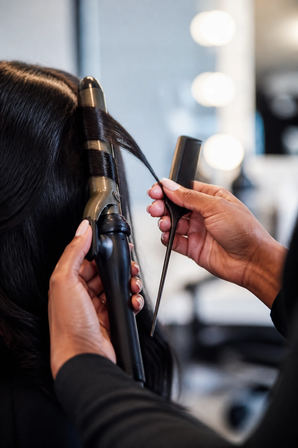 Hands holding curling iron and rat-tail comb in a salon setting