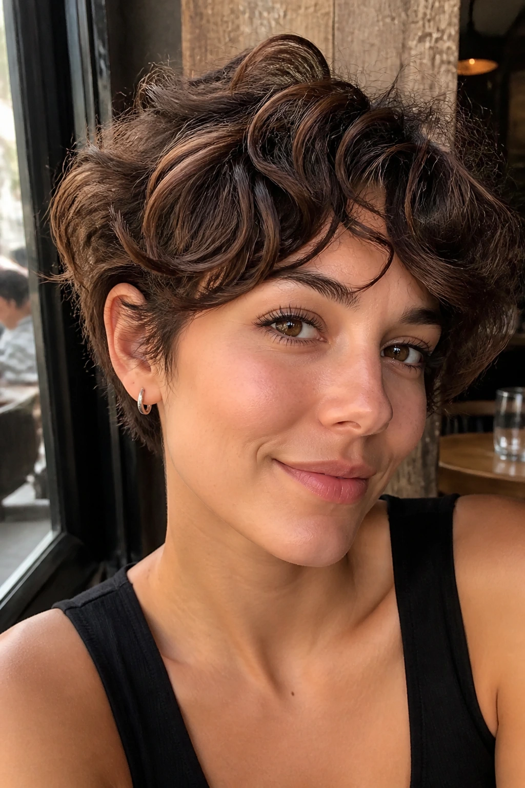 Real woman with curly bixie hairstyle and deep brunette lowlights in a sunlit cafe setting
