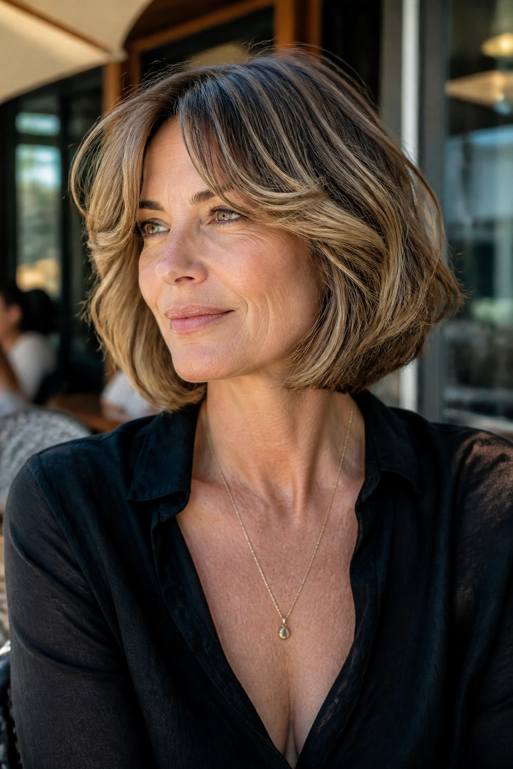 Portrait of a woman with curved-under bob and bouncy curtain bangs in outdoor cafe light