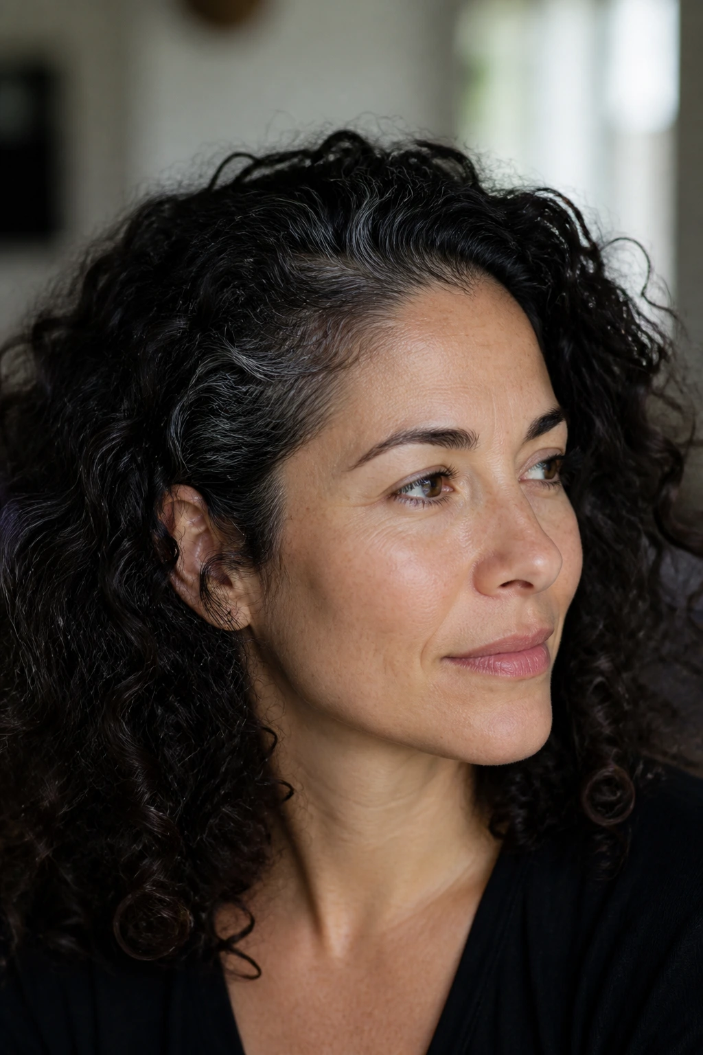 Portrait of a dark curly-haired person with subtle gray strands in curls