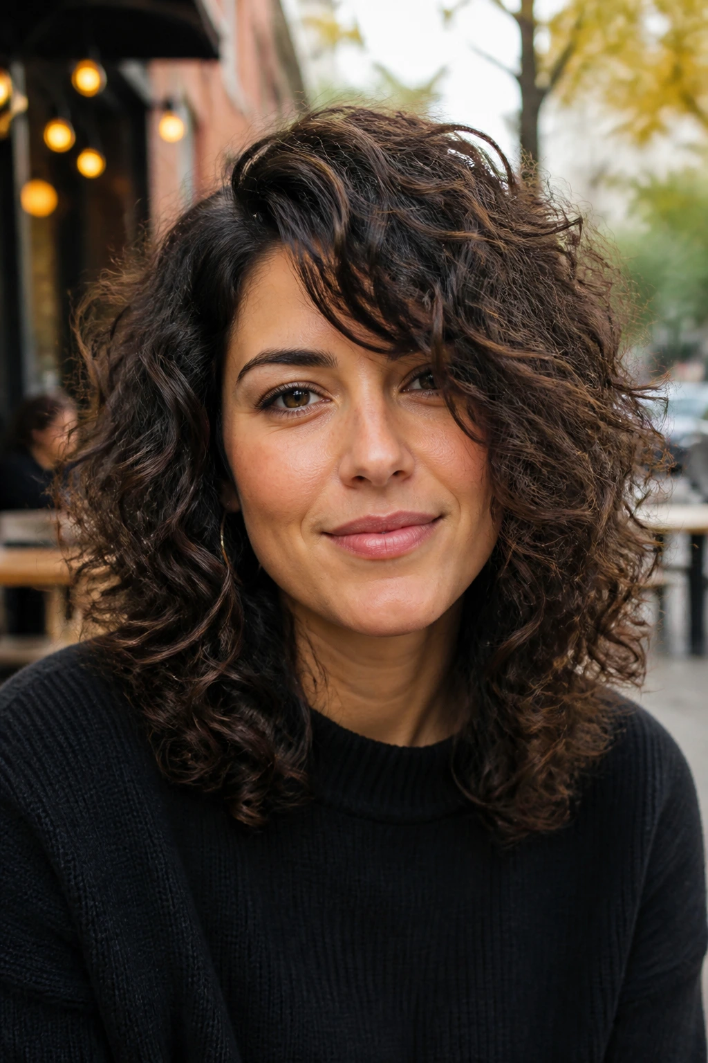 Close-up of a real person with layered Deva cut and side-swept fringe in a cafe setting.
