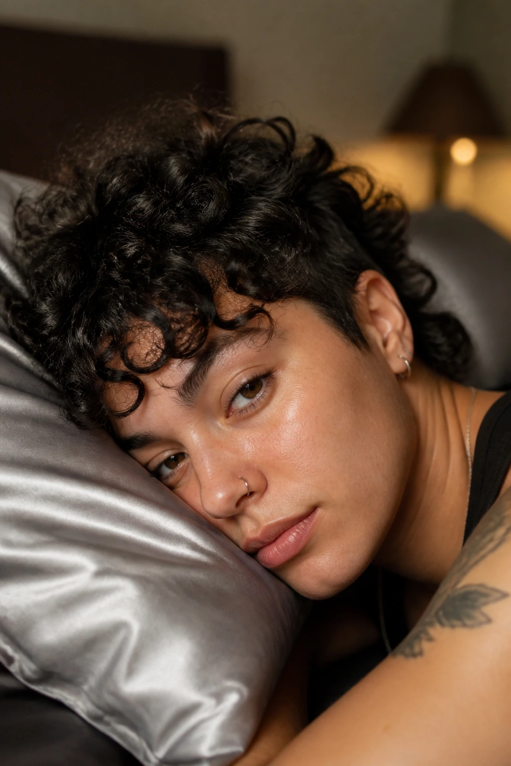 Person with curly hair resting on satin pillow in bedroom
