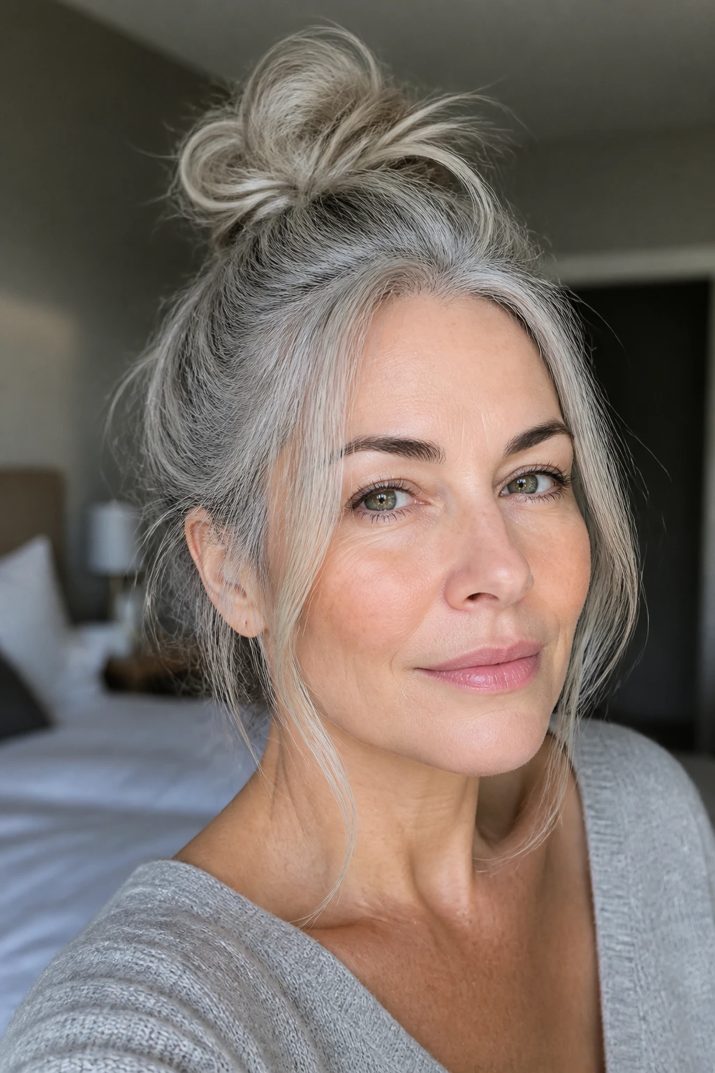 Close-up of a real woman with a messy top knot and loose face-framing pieces in gray hair