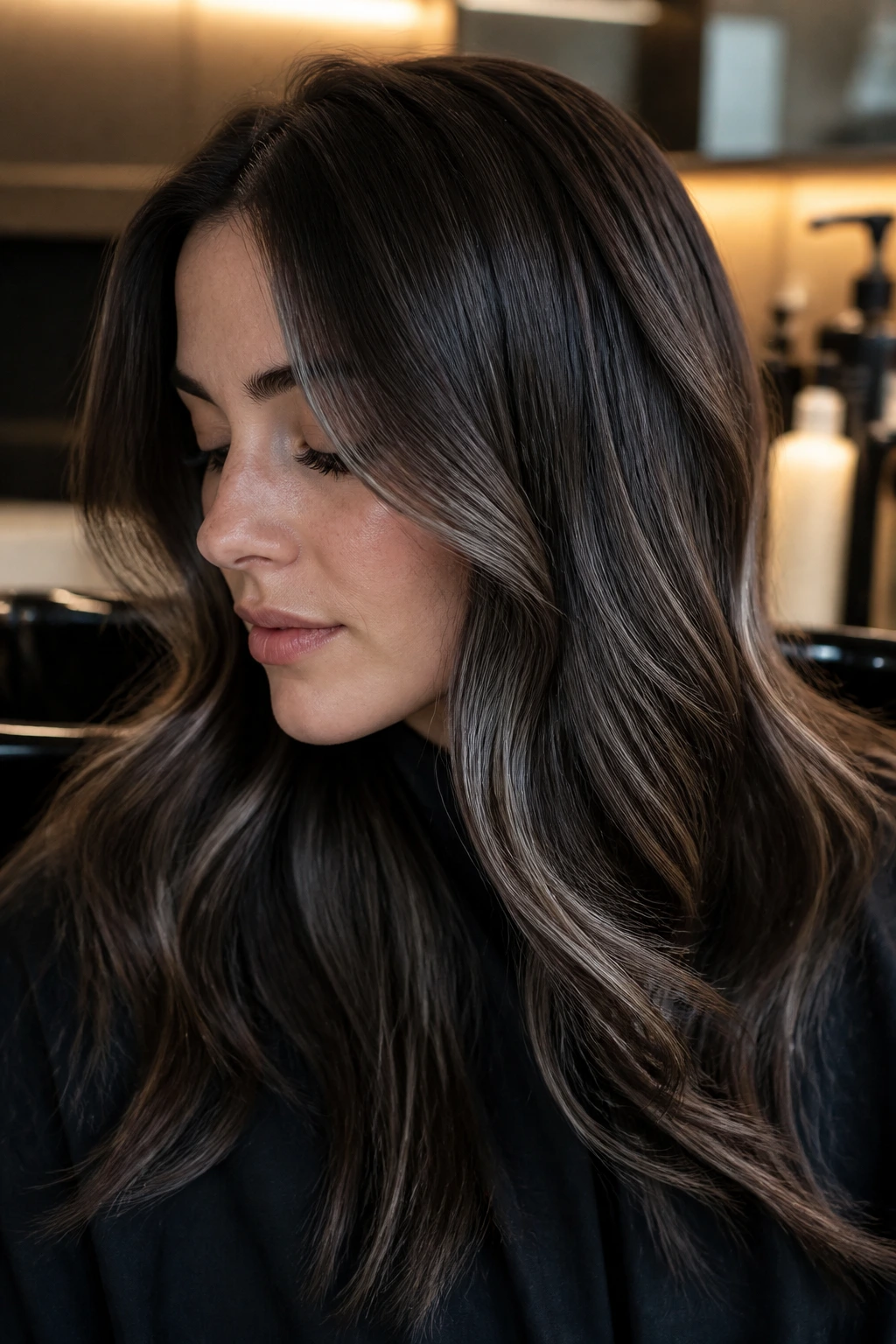 Close-up portrait of a person with dark brown hair and subtle grey balayage in a salon