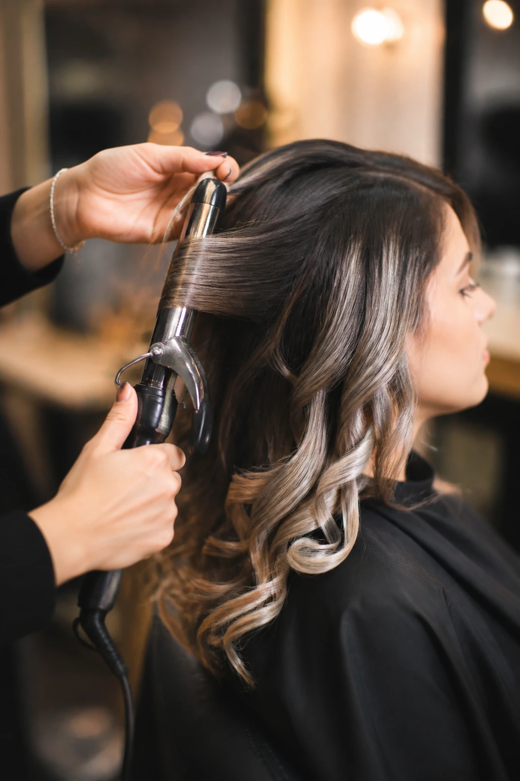 Hands holding a curling iron styling hair on a real client in a salon