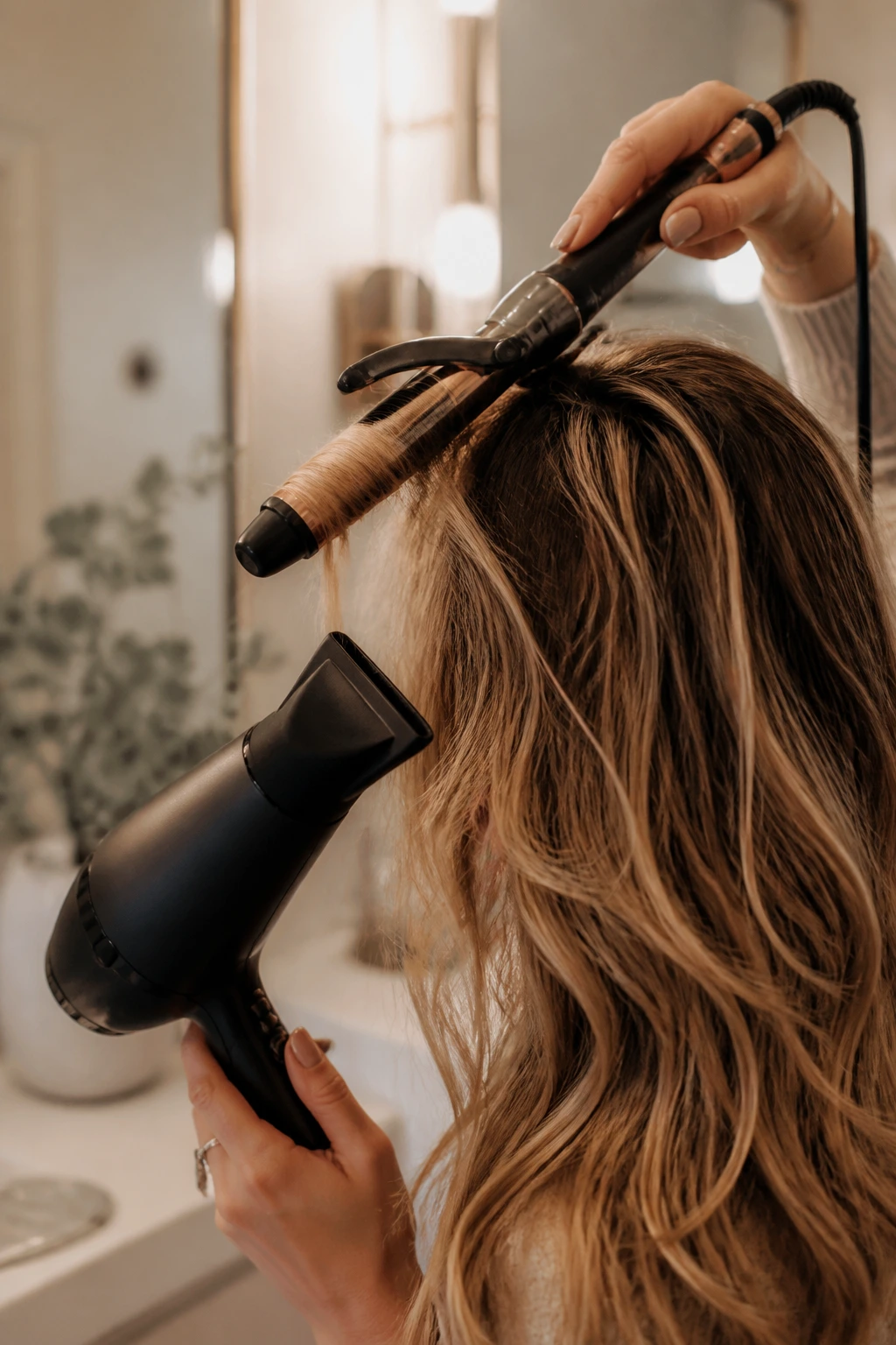 Hands using curling iron with hair being styled, showcasing essential hair styling equipment