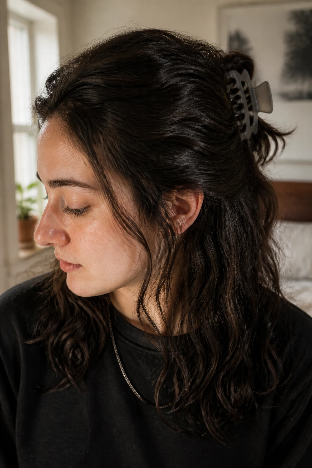 Close-up of a real person with thick hair in a half-up sweep secured by a large claw clip, warm bedroom morning light