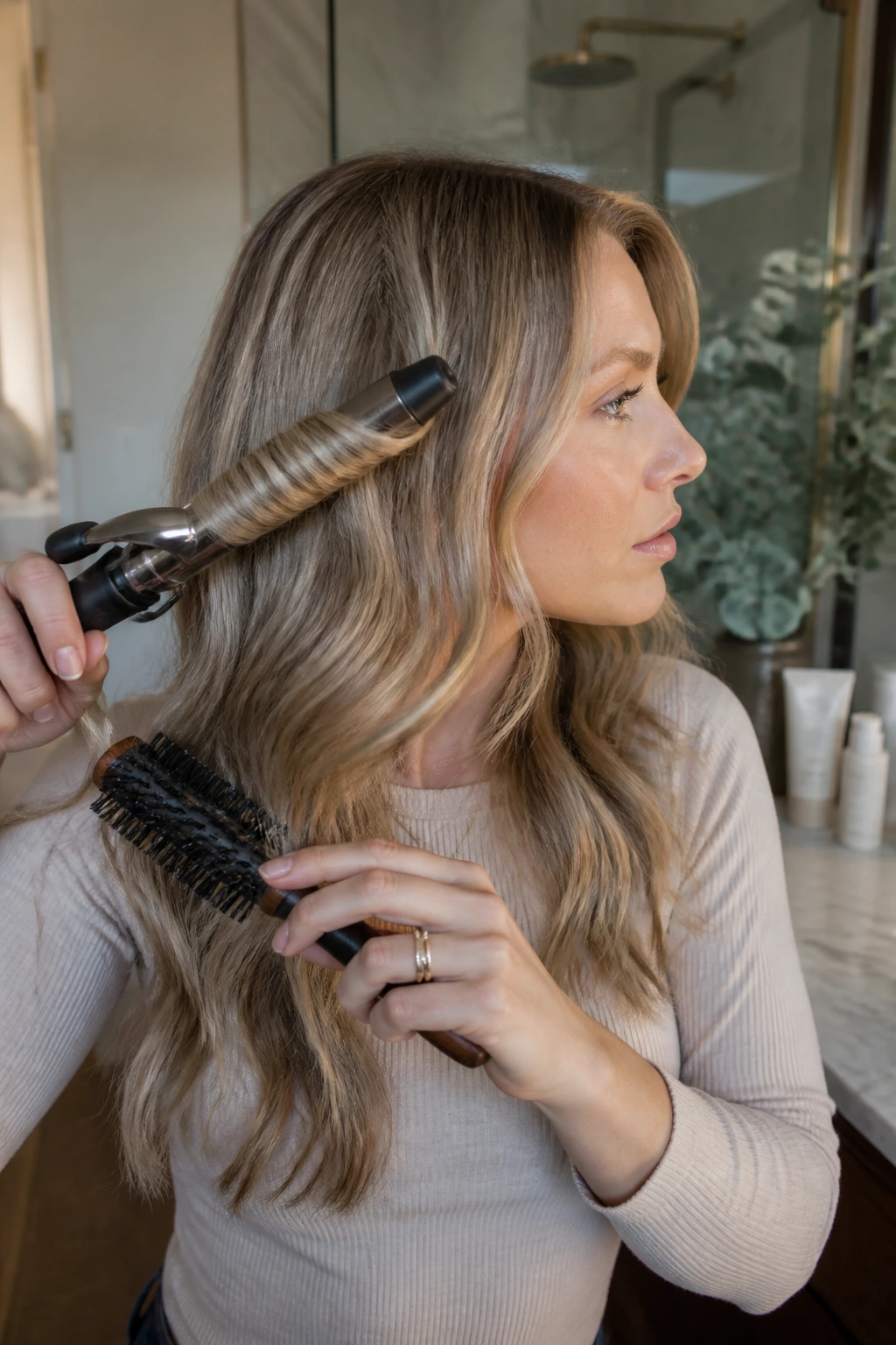 Portrait of a person styling hair at home with a brush and curling iron