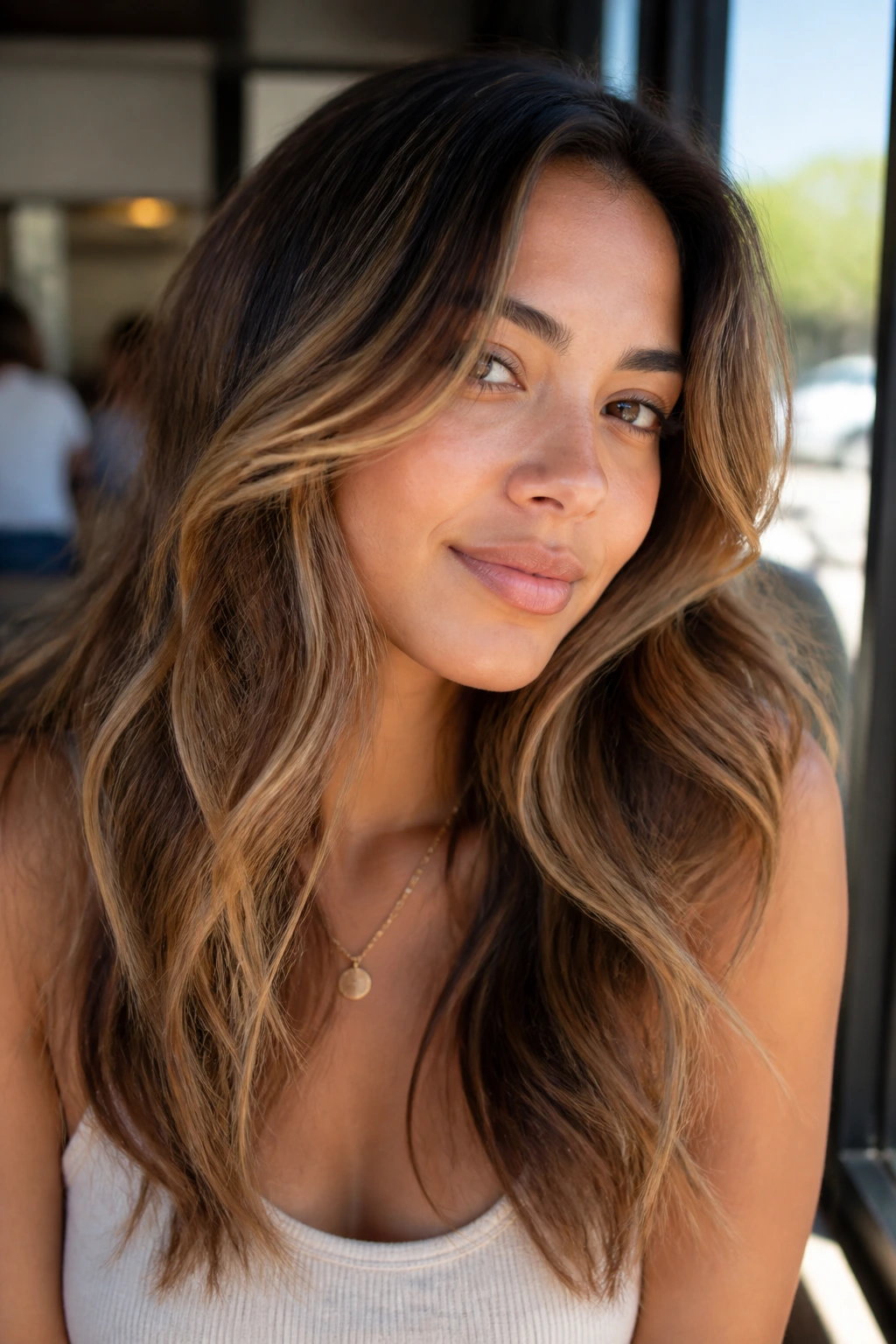 Portrait of a person with multi-tone honey and caramel highlights outdoors near a cafe.
