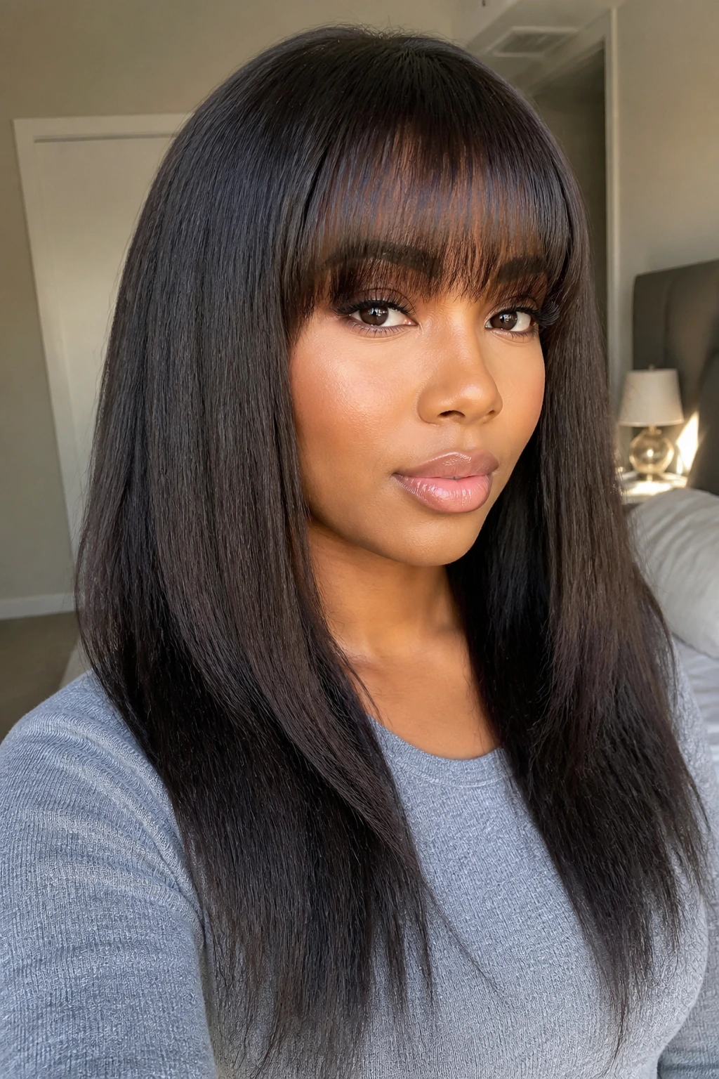 Close-up of a real woman with kinky straight blowout and rounded full bangs in a softly lit bedroom