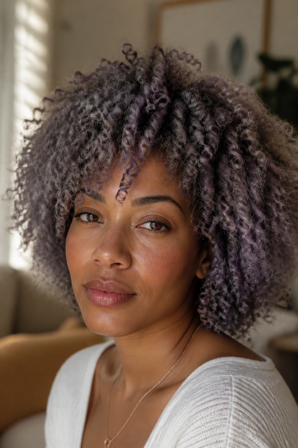 Close-up portrait of a real person with hazy lavender grey curls and muted lowlights in a cozy setting