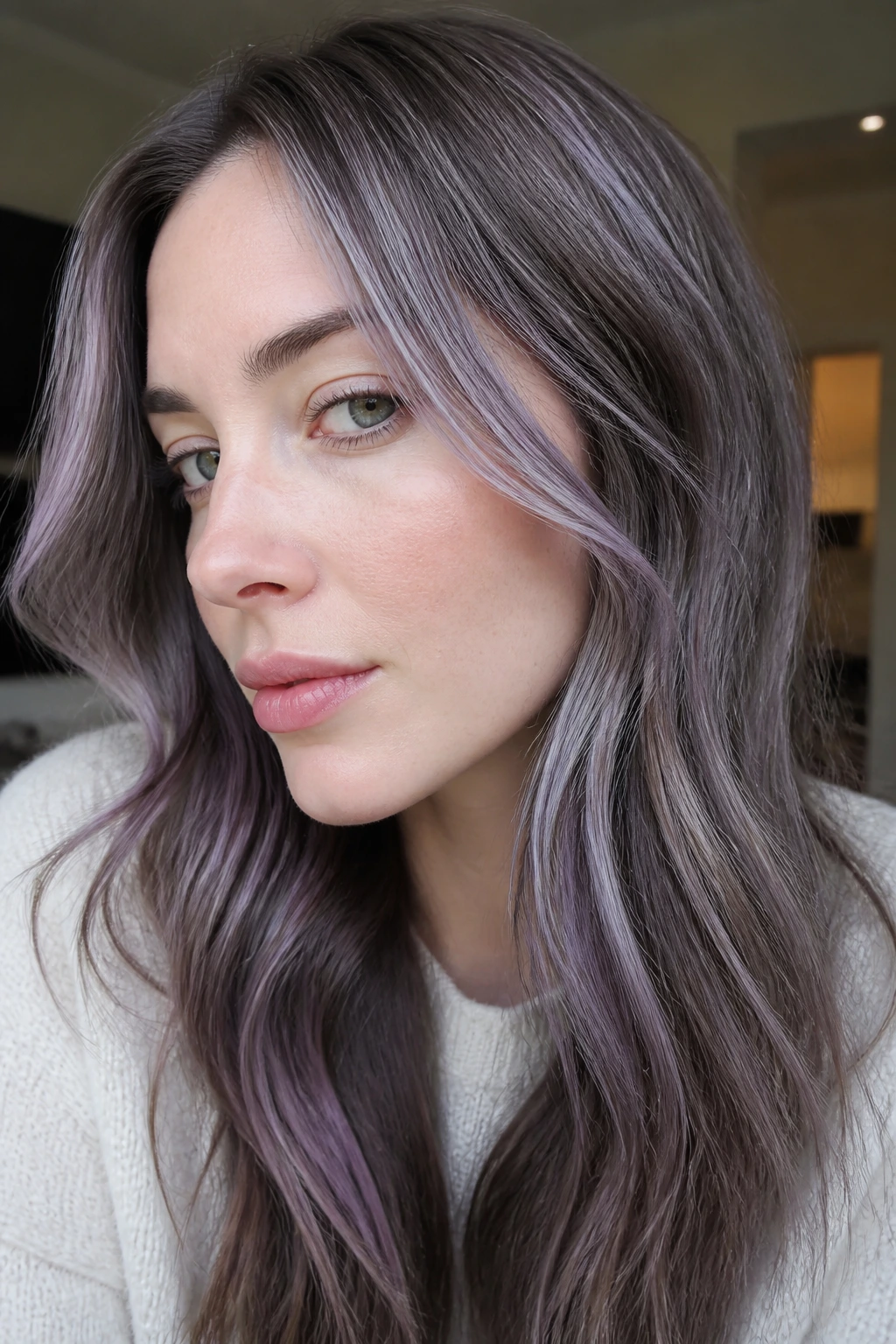 Close-up of lavender-tinted grey streaks through long hair on a real person in a modern interior.