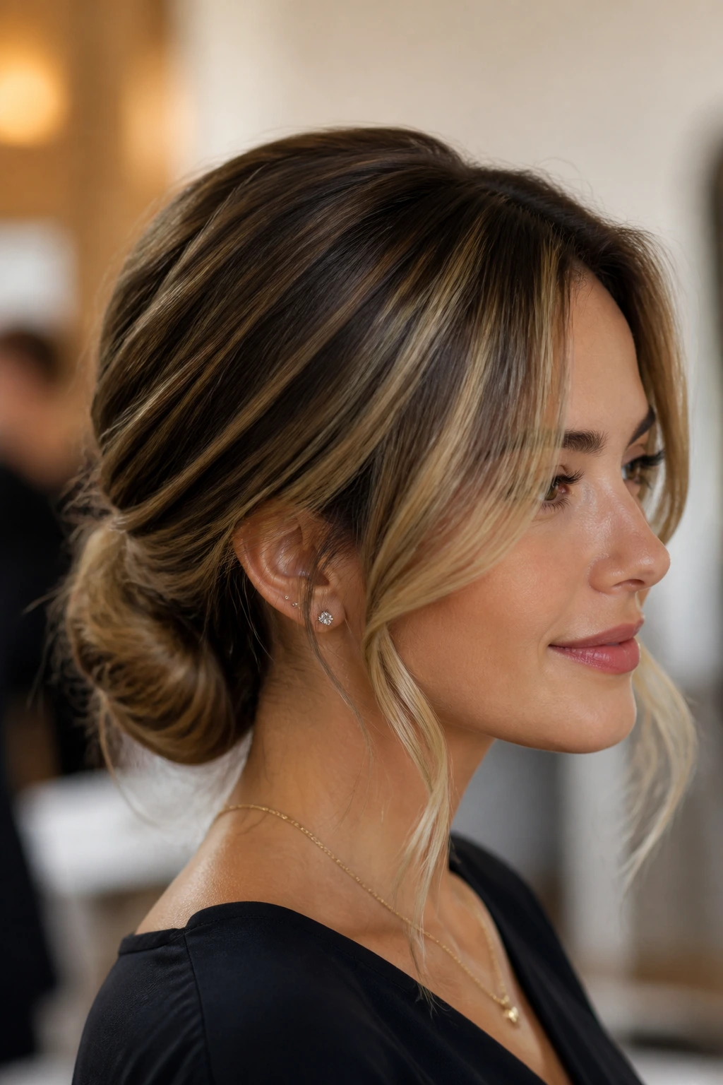 Close-up of real woman with a low chignon and face-framing strands in brunette hair with blonde highlights