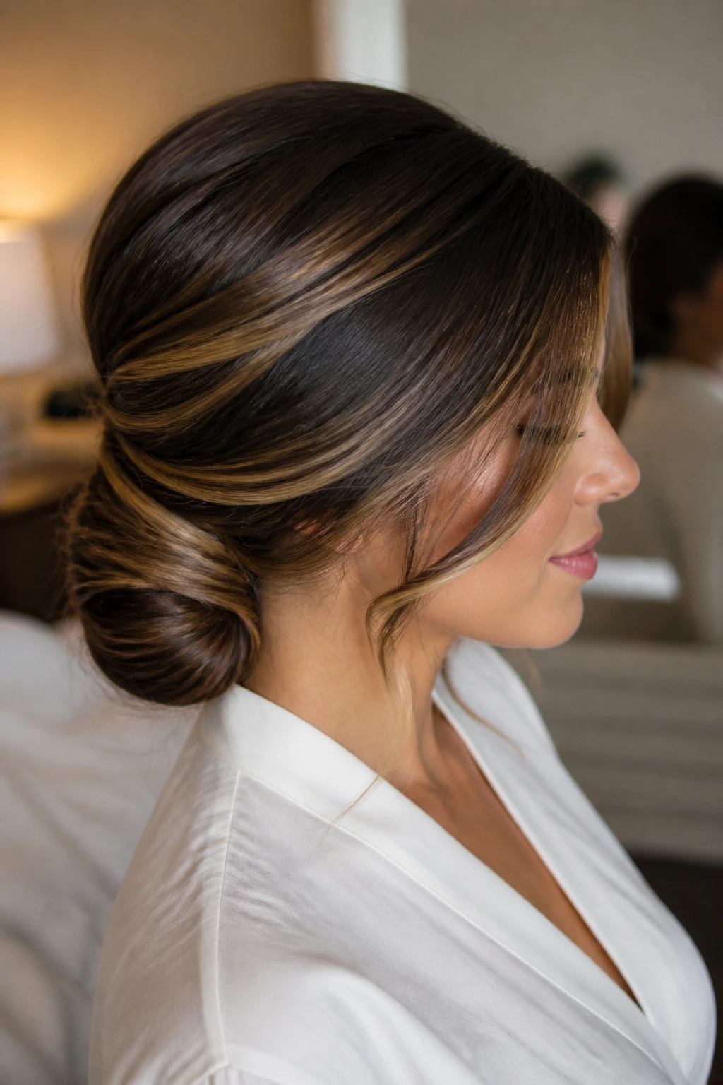 Close-up of a low chignon with side-swept face pieces and caramel highlights on a real person