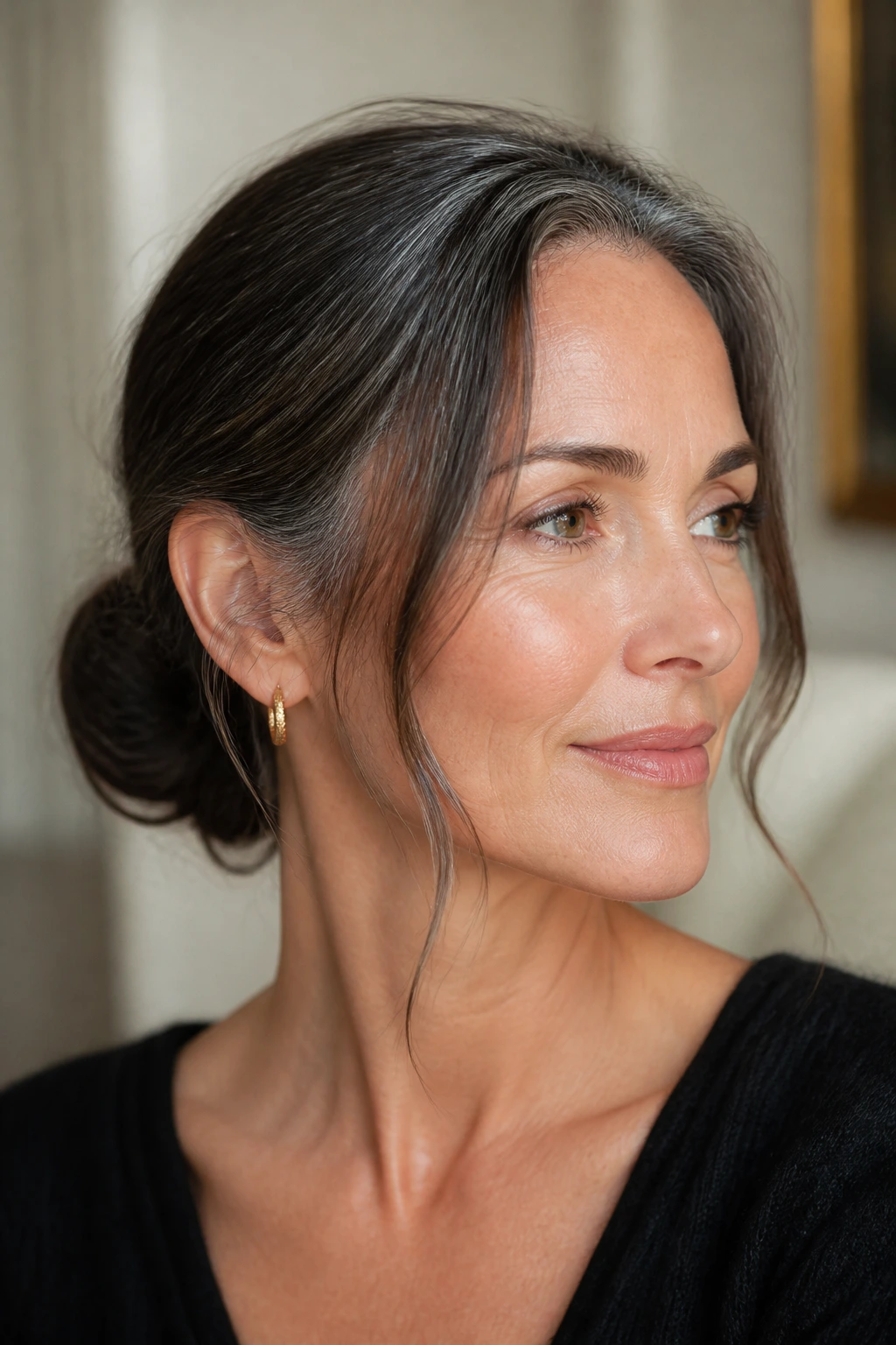 Close-up brunette with low chignon and wispy temples in soft light.