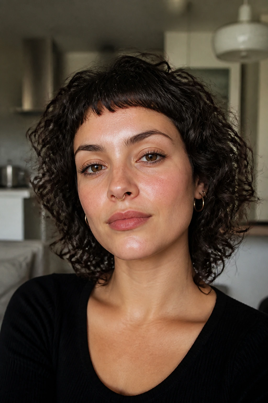 Close-up of a real person with micro bangs and curly hair in a softly lit room