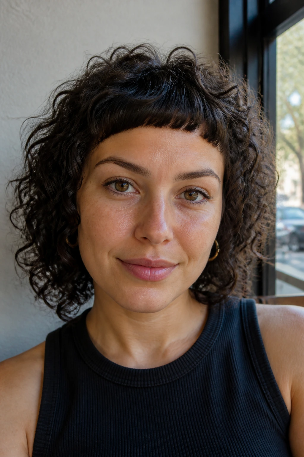 Close-up of a real woman with micro curly fringe in cafe daylight