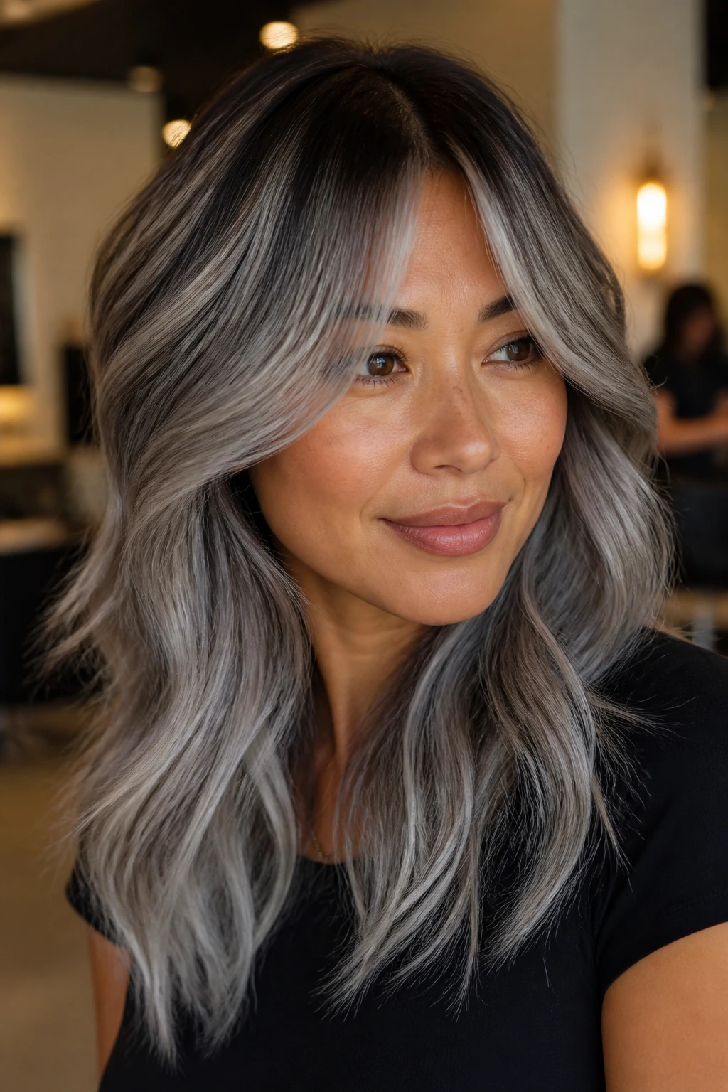 Close-up of a real woman with pewter balayage and soft root shadow, curtain bangs