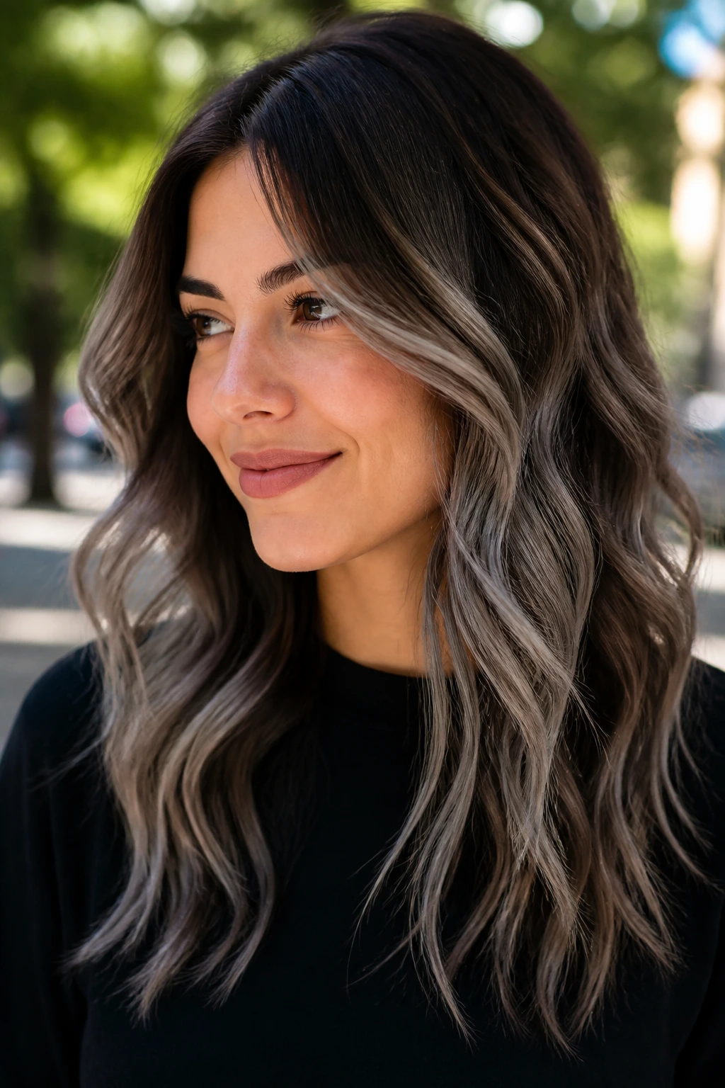 Brunette with pewter balayage on wavy lengths in natural outdoor light