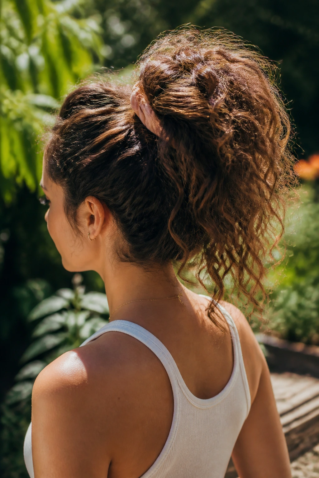 Three-quarter back view of woman with high pineapple ponytail lifting crown and fanning curls
