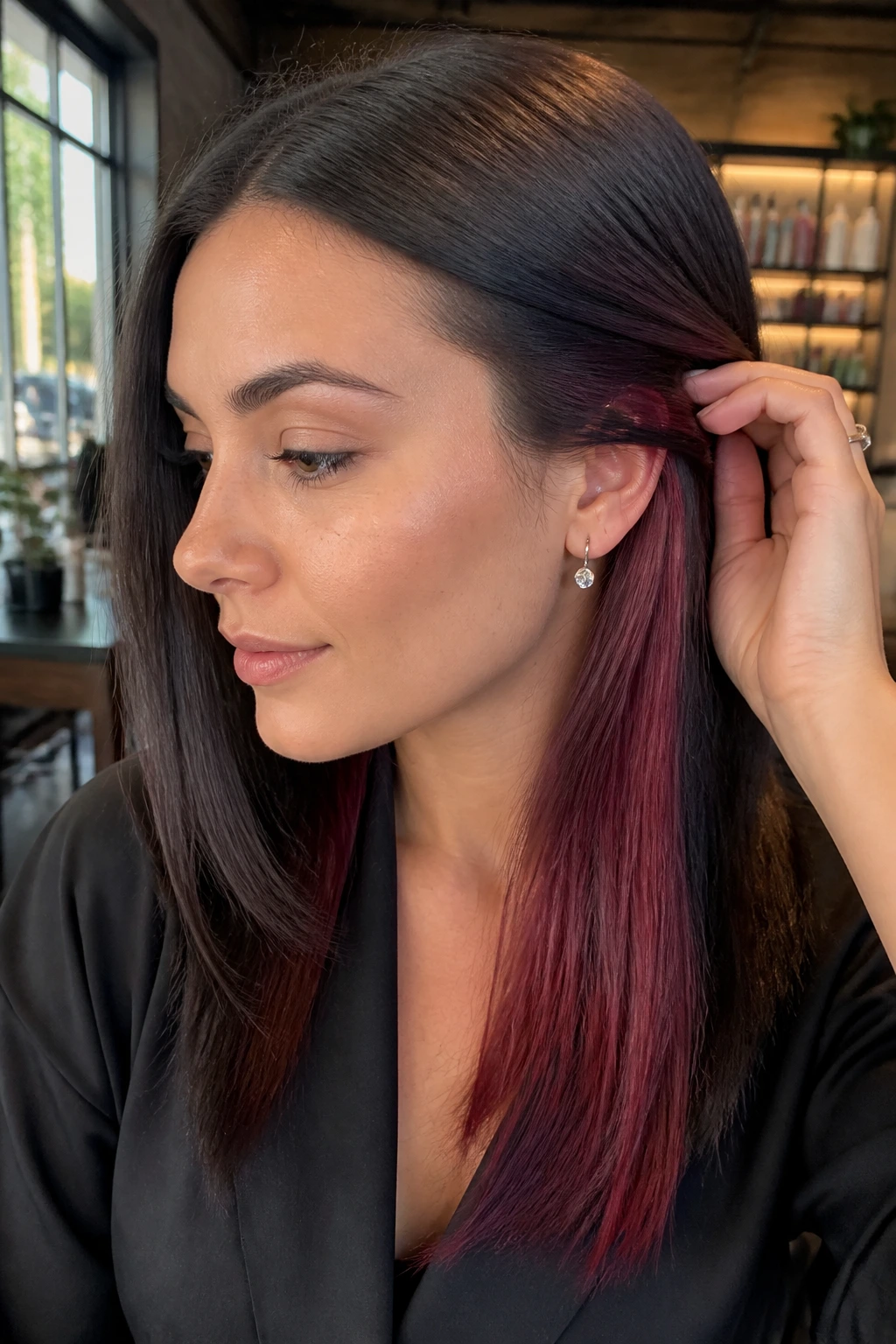 Close-up of red velvet peekaboo highlights under straight hair on a real woman in a softly lit salon