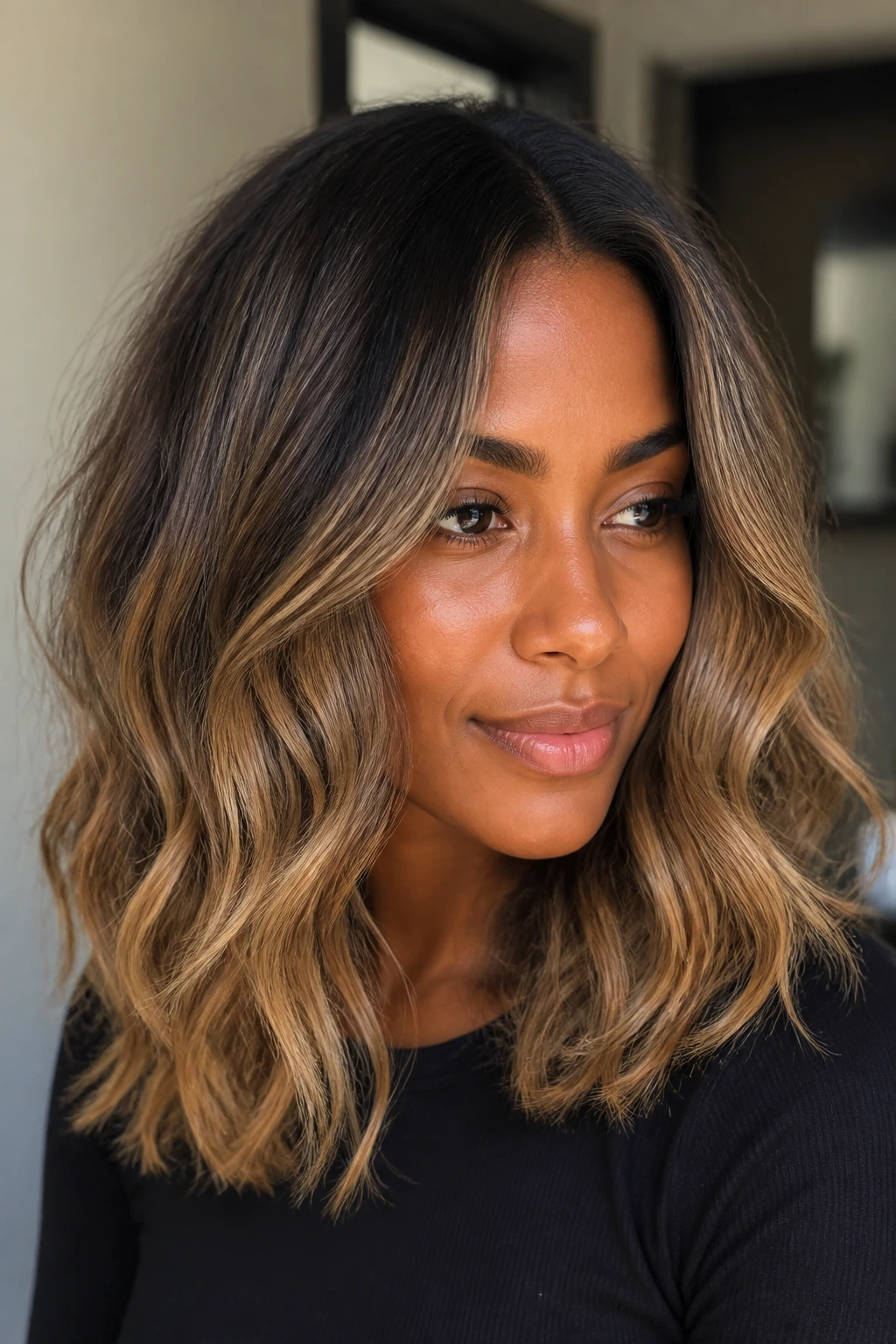 Close-up of a real woman with mid-length hair featuring root smudge and caramel mids.