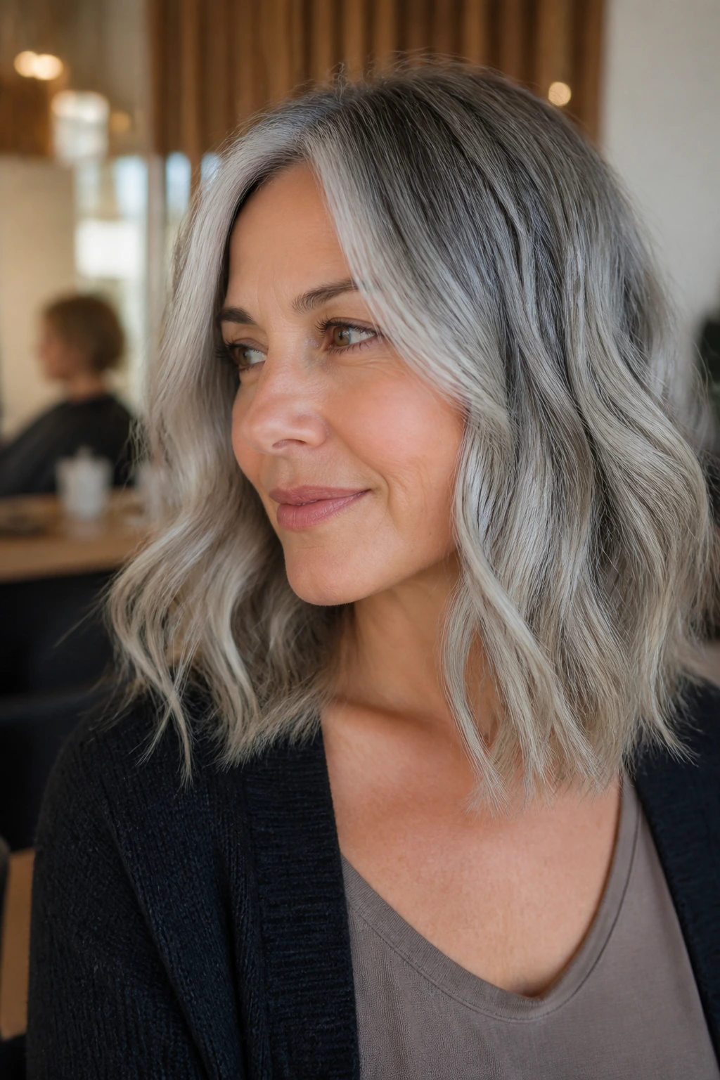 Close-up of real woman with rooted grey wavy lob and warm skin tone.