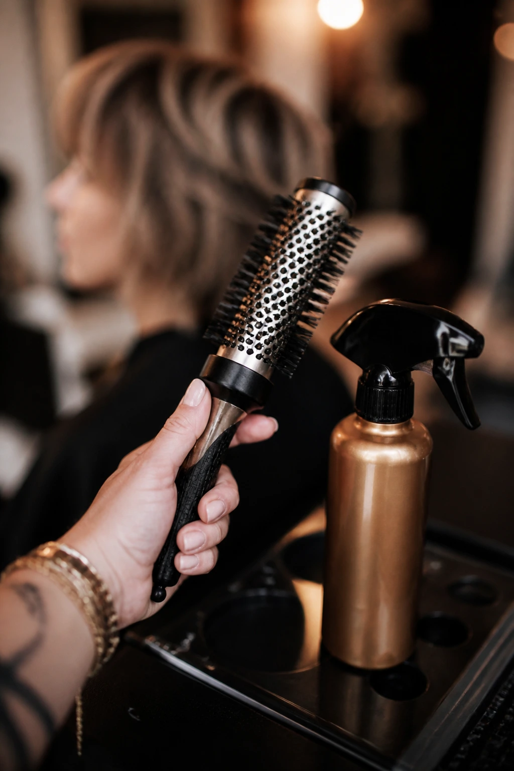 Close-up of styling tools (round brush and spray bottle) in a salon setting.
