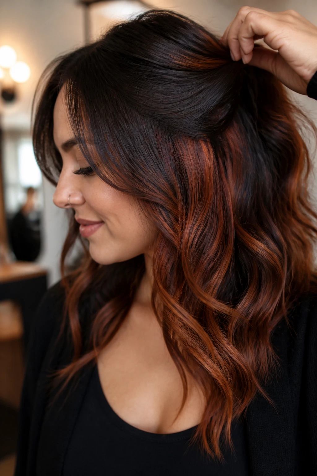 Close-up of a real woman with dark hair and rust underlayers peeking through wavy hair in a salon setting