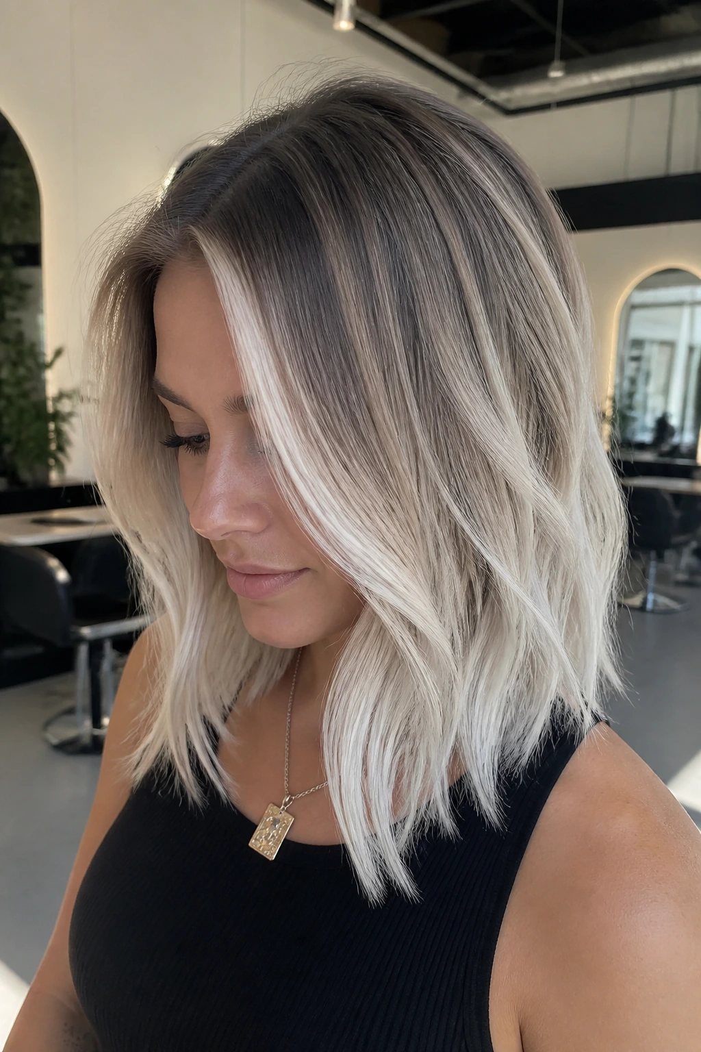 Real woman with shadow-root melt showing dark roots and icy platinum ends on shoulder-length hair.