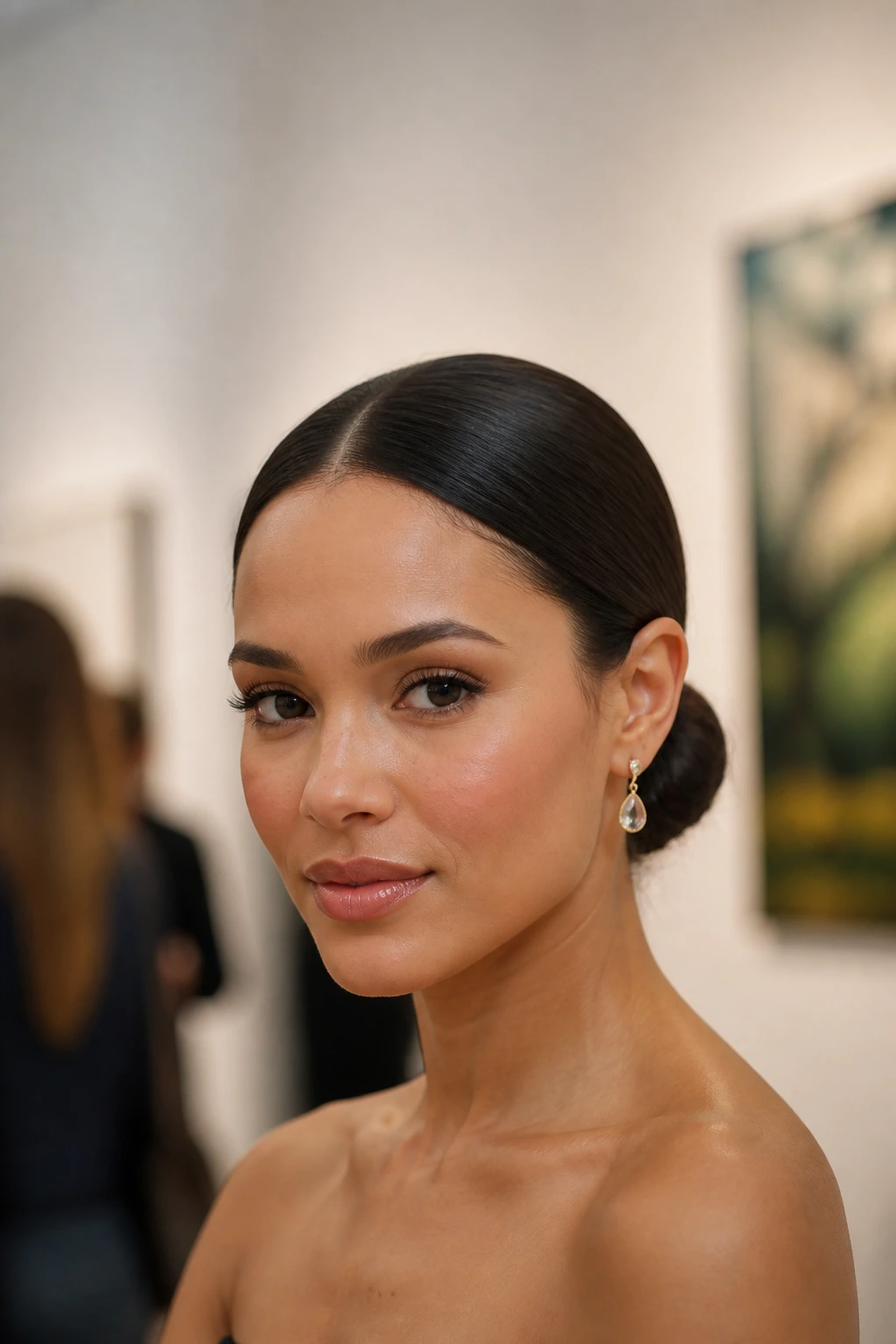 Portrait of a real person with a sleek center-part low bun at the nape in a gallery setting.