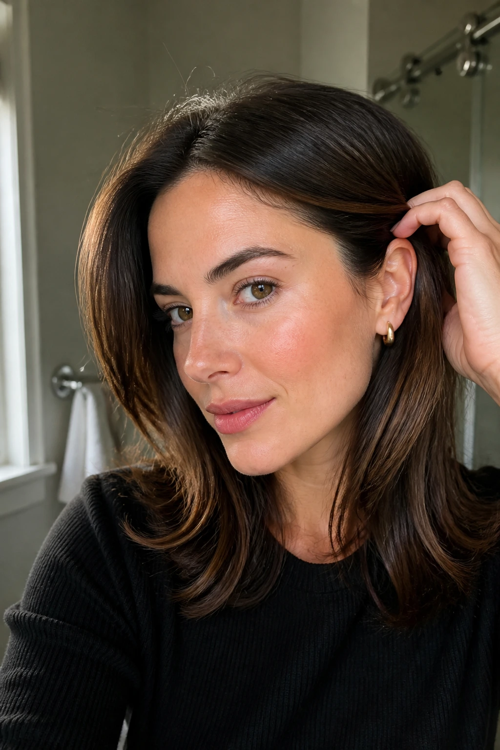 Close-up of a real woman showing small styling moves: ear tuck and subtle part shift with shiny ends and matte roots.