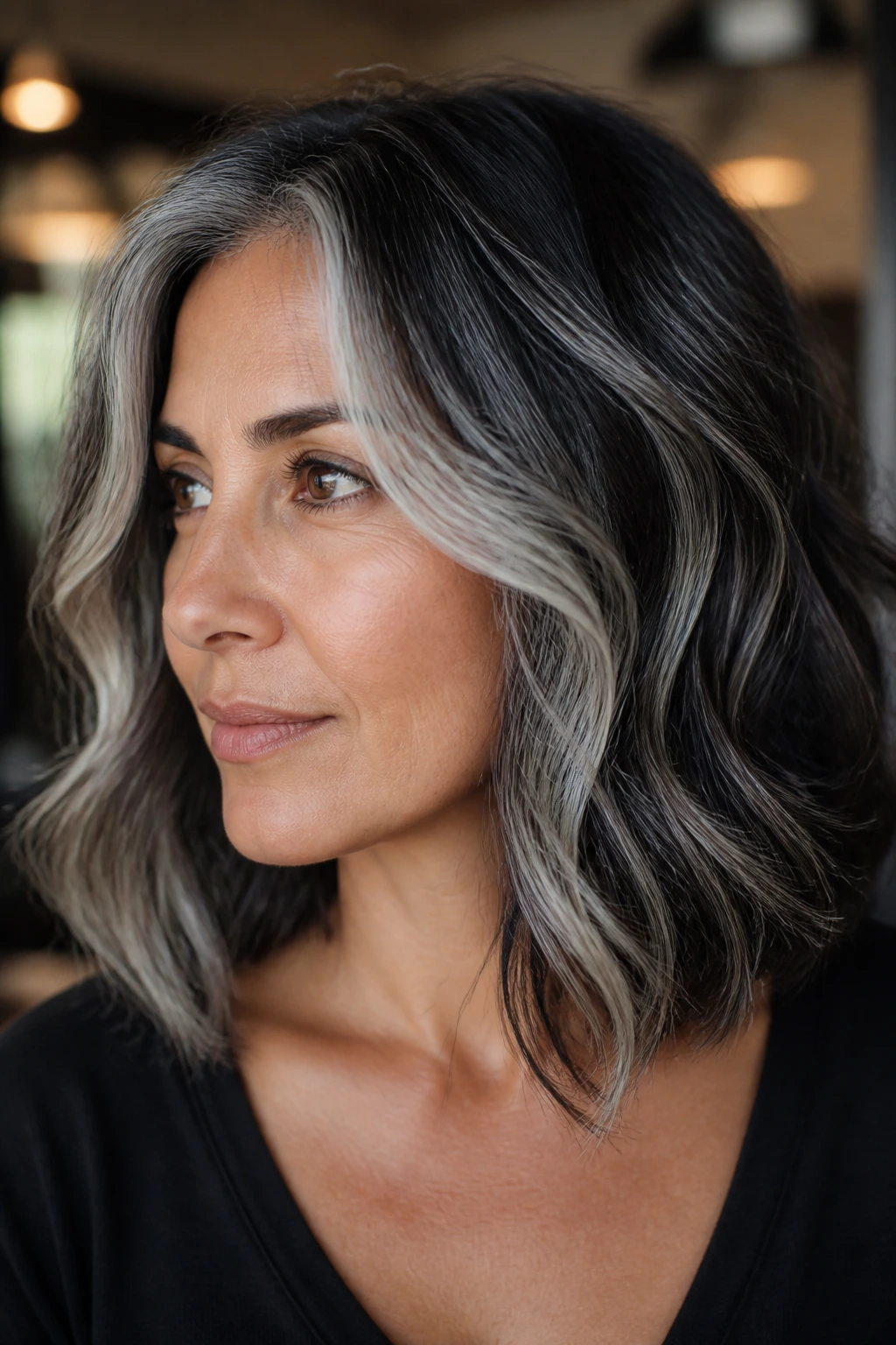 Close-up portrait of a real person with storm-cloud balayage hair in moody salon lighting