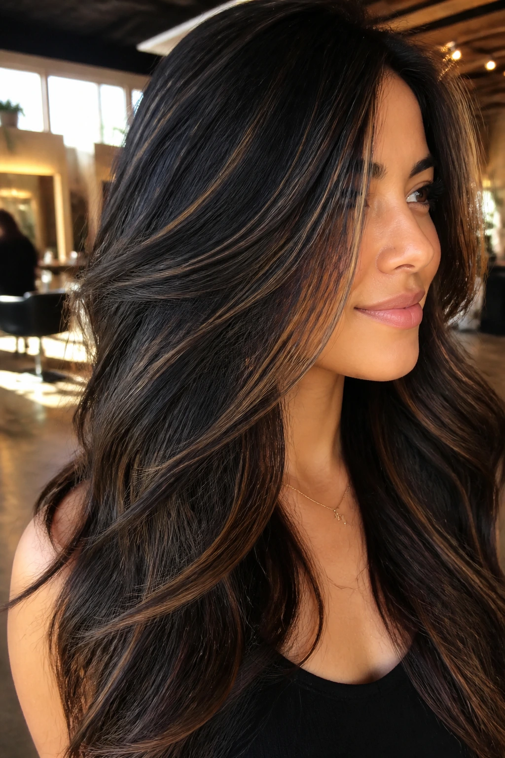 Close-up of thick dark hair with caramel highlights on a real person in a warm salon setting