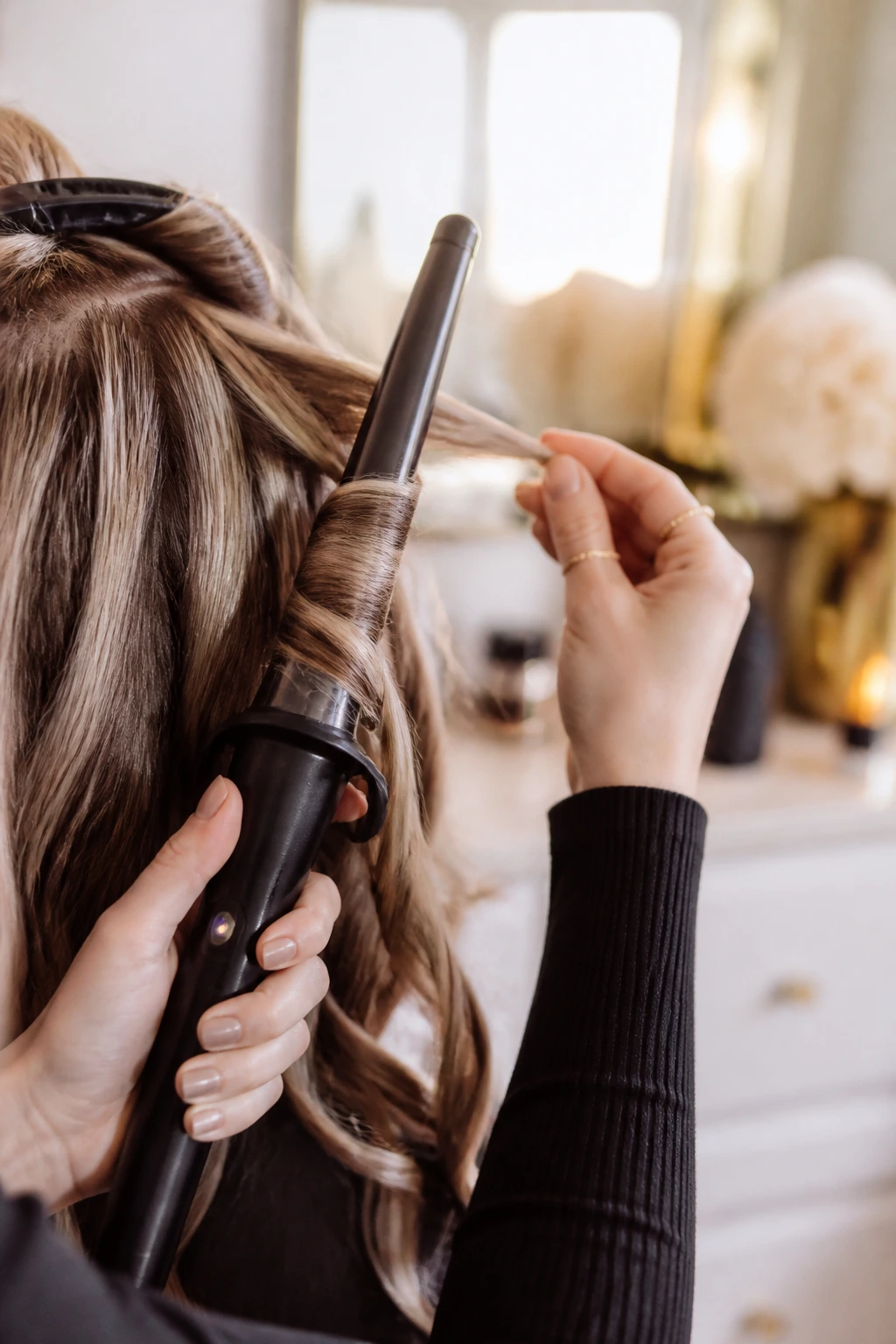 Hands holding curling wand with hair lift in bright setting
