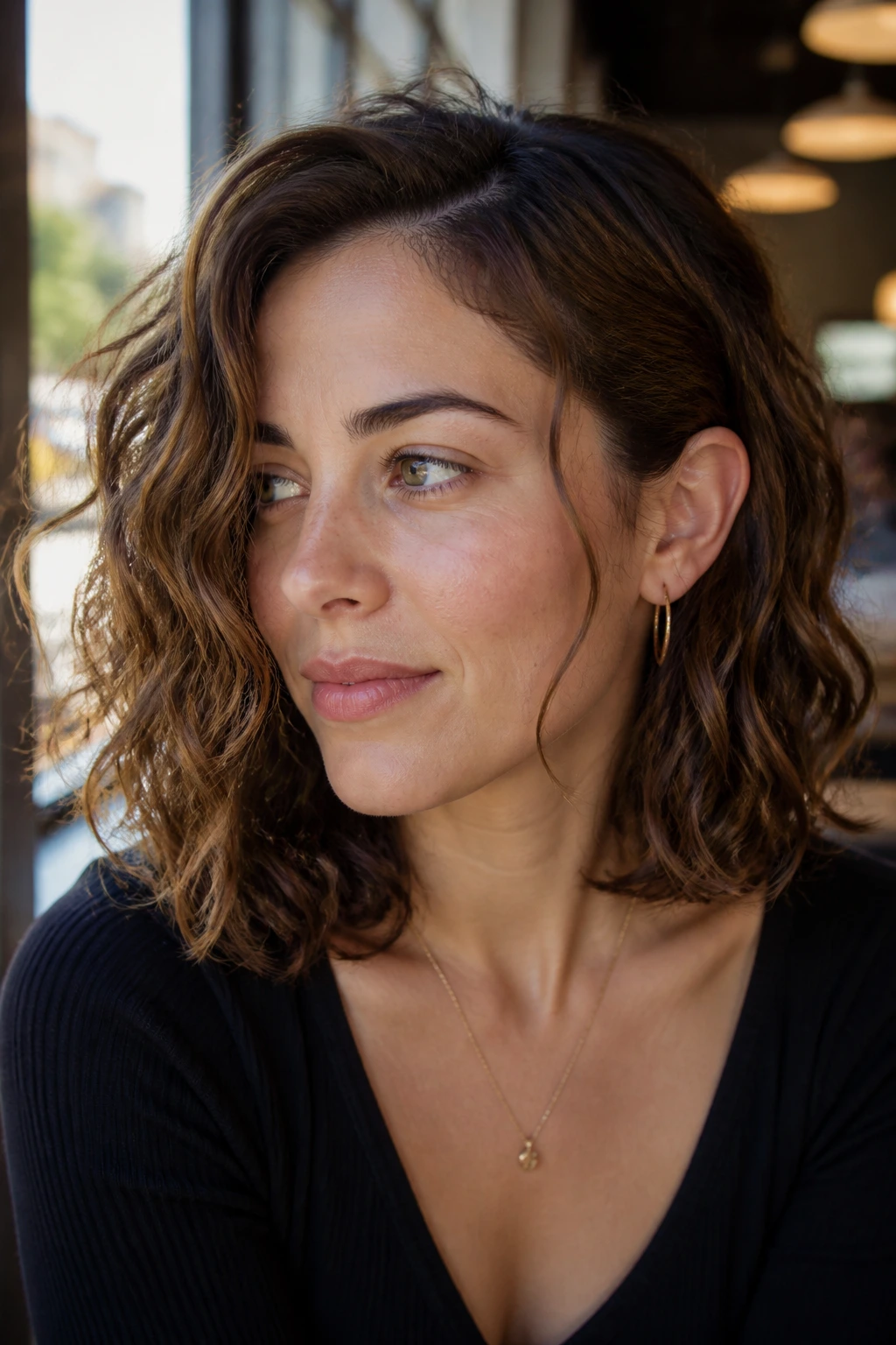 Close-up of woman with tucked-behind-ear lob hairstyle in sunlit cafe