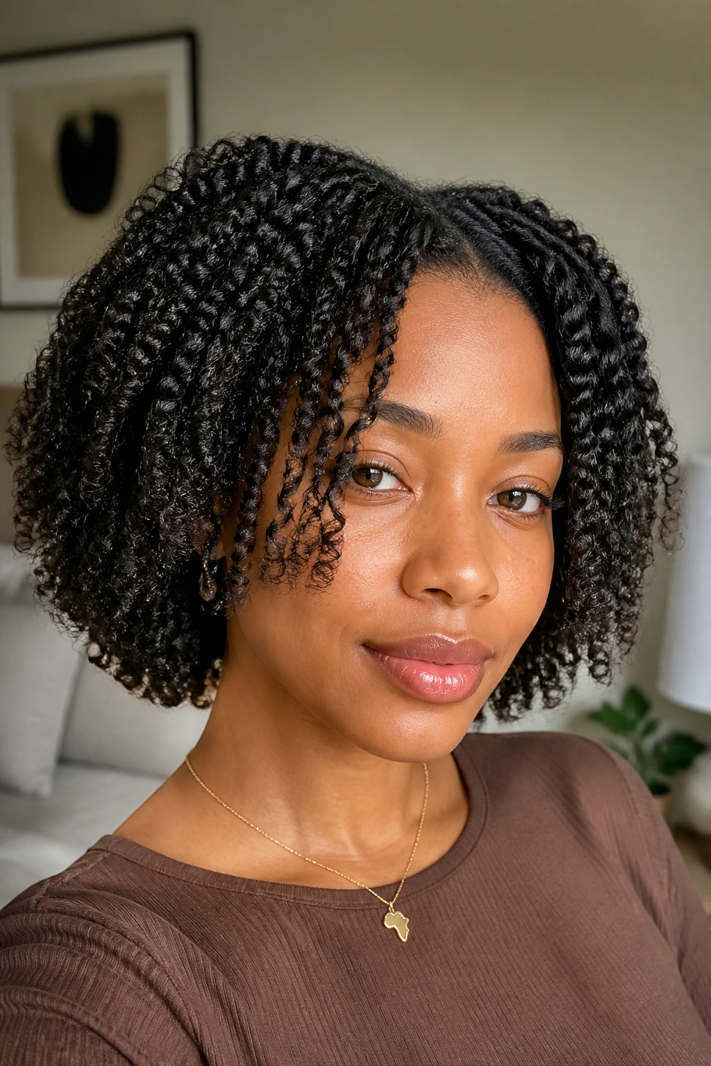 Close-up portrait of a real Black woman with a layered twist-out framing the face in a bright bedroom